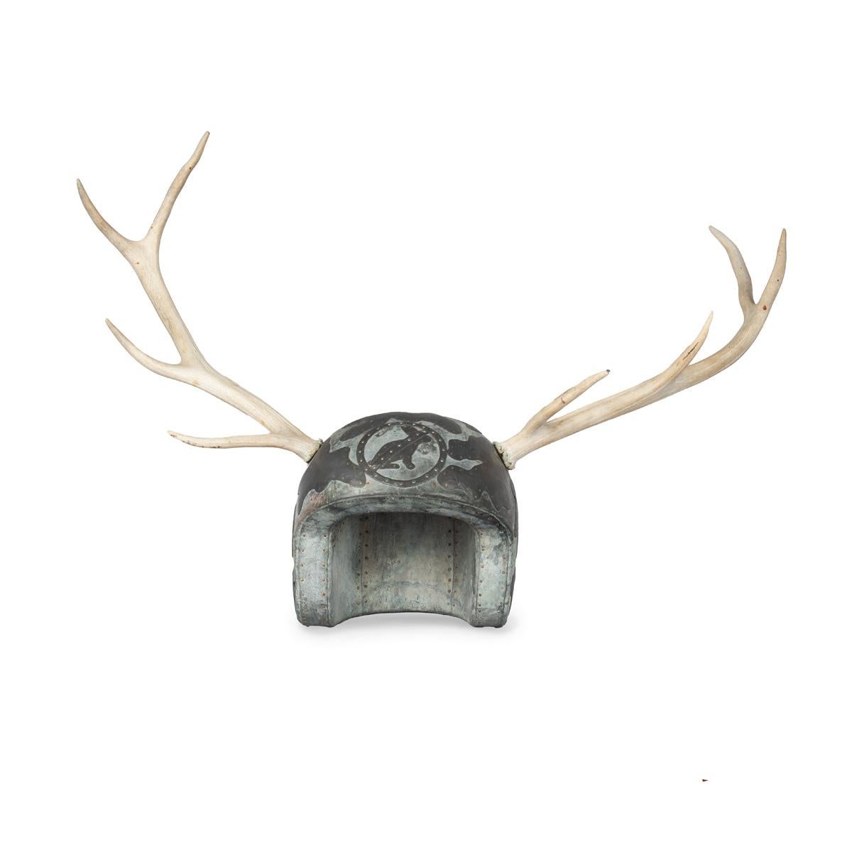Un grande casco in metallo con corna di cervo applicate di Martin Scorey, la forma in legno ricoperta da fogli di metallo inchiodati e decorati con forme astratte di nuvole, un distintivo CND e un cartello stradale che racchiude un coniglio con un
