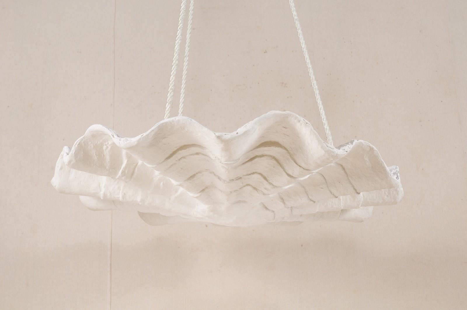 This artisan-made hanging modern light fixture, inspired by midcentury designs, has an overall convex and rounded shape, with undulating waves and concentric ring textures adorning it's downward-facing facade. This handcrafted plaster light fixture,