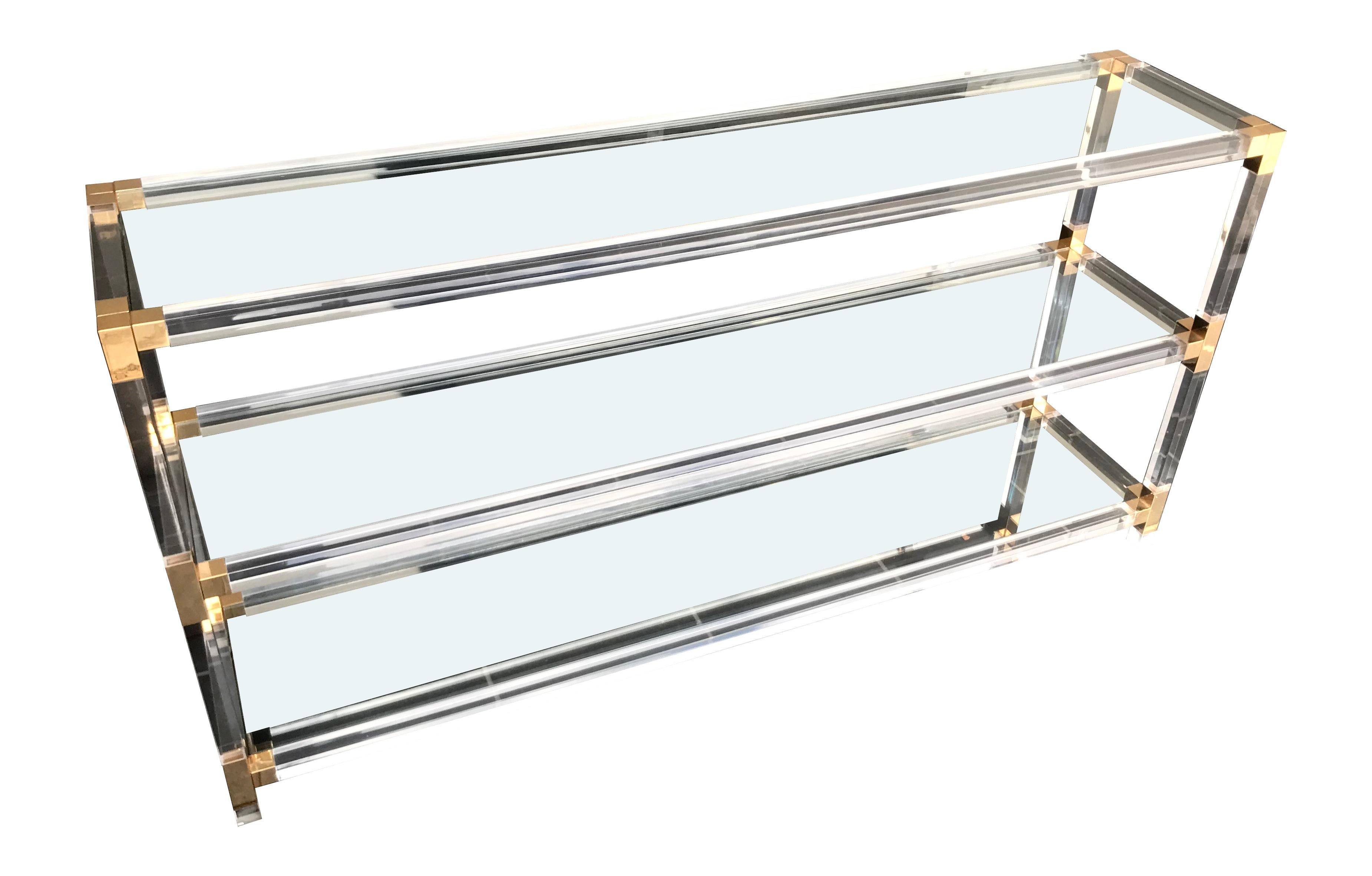 A large midcentury Lucite console table with three clear glass shelves and gilt metal corners and joints.