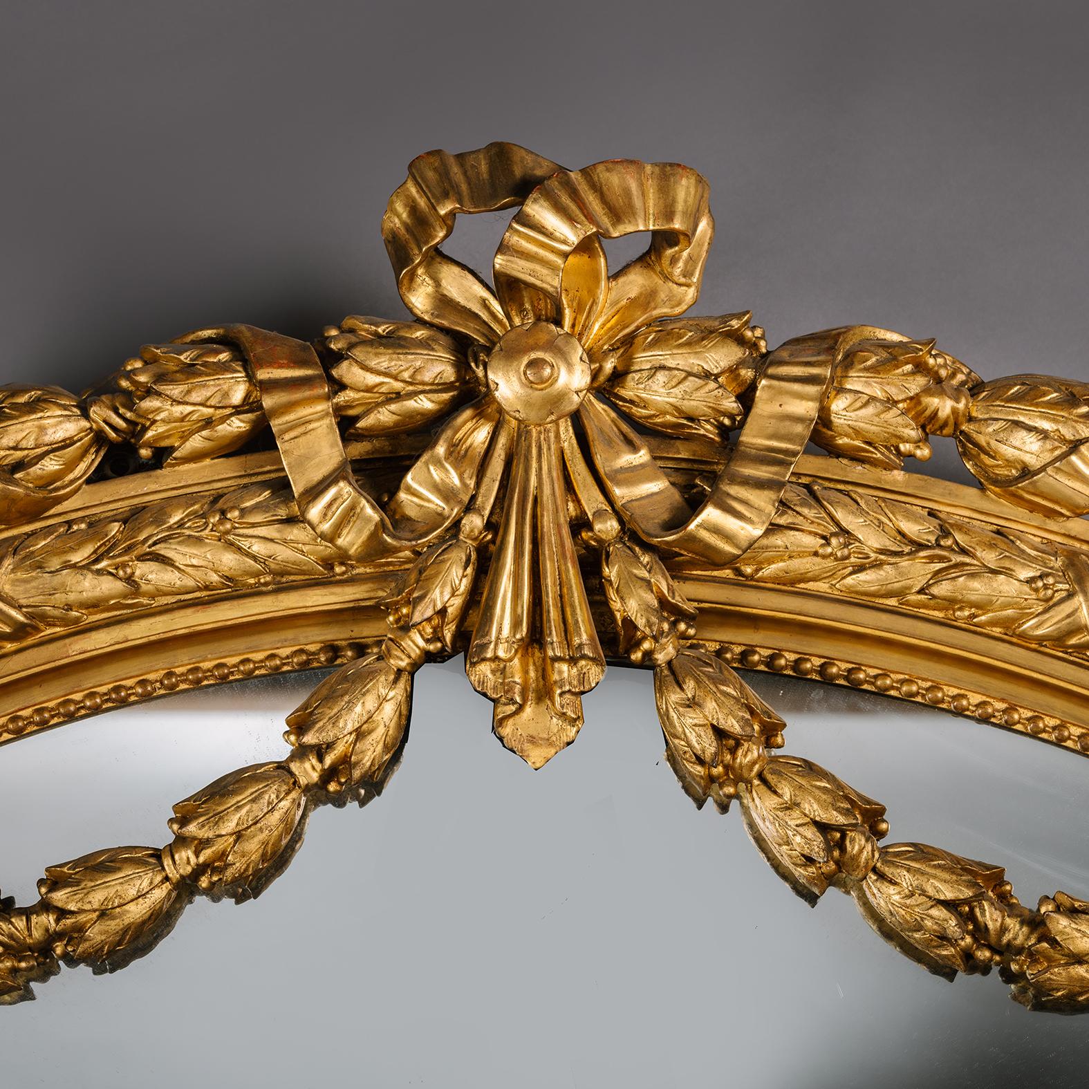 A Large Napoleon III Carved Giltwood & Gesso Mirror. 

Grand in size and decoration, this impressive Napoleon III period overmantel mirror is designed in the Louis XVI style with an arched pediment centred by an elaborate ribbon tied cresting