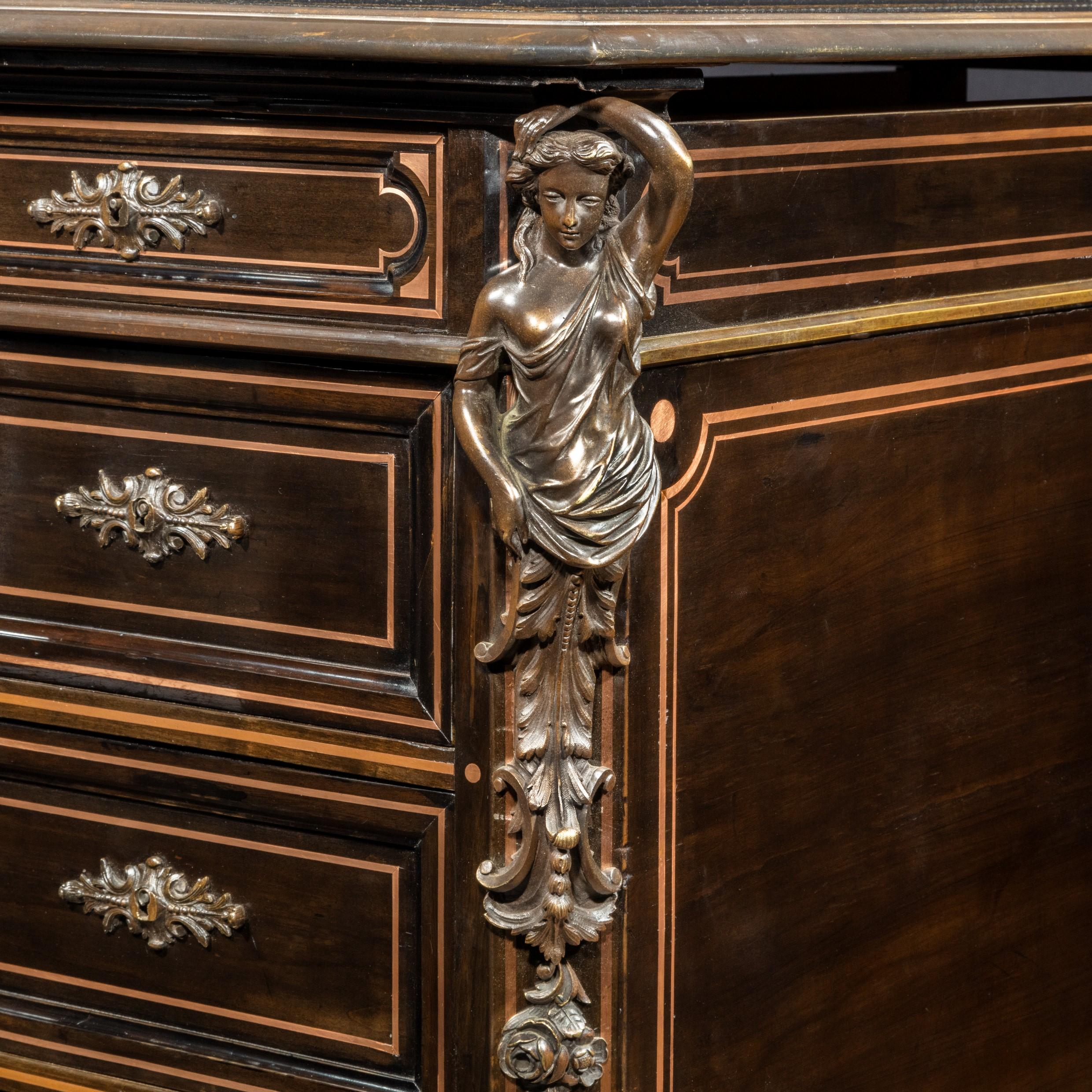 A large Napoleon III ebonized partners’ desk, the rectangular leather inset top with copper stringing and a matching book slide at either end, each side with one long and two short drawers above two pedestals enclosing drawers, cupboards with
