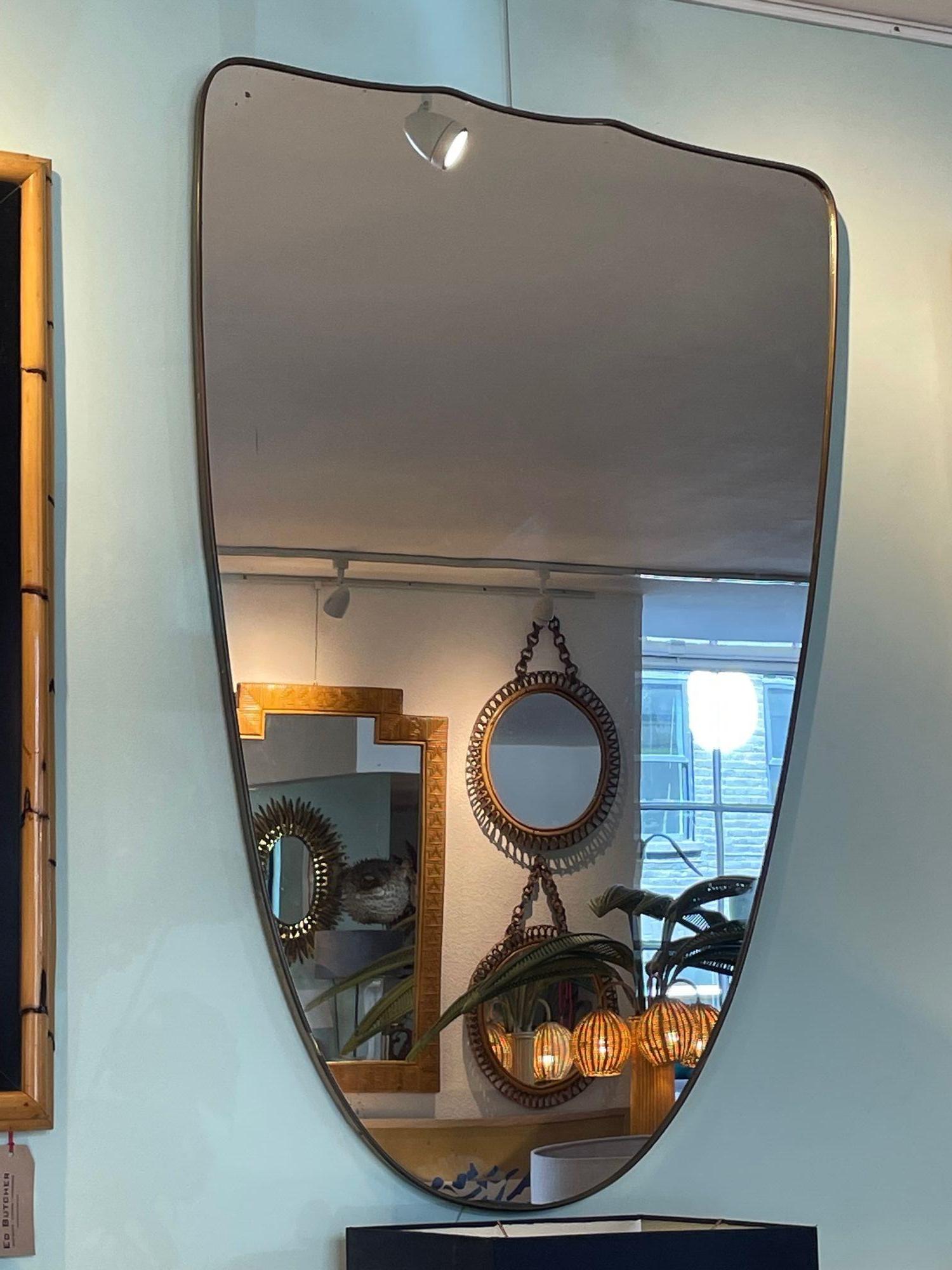 A large orignal Italian 1950s shield mirror with thick brass frame and orignal plate with solid wood back. The overall condition is good with some small spots of foxing on the orignal plate, which is consistent with its age. See last 3 photos