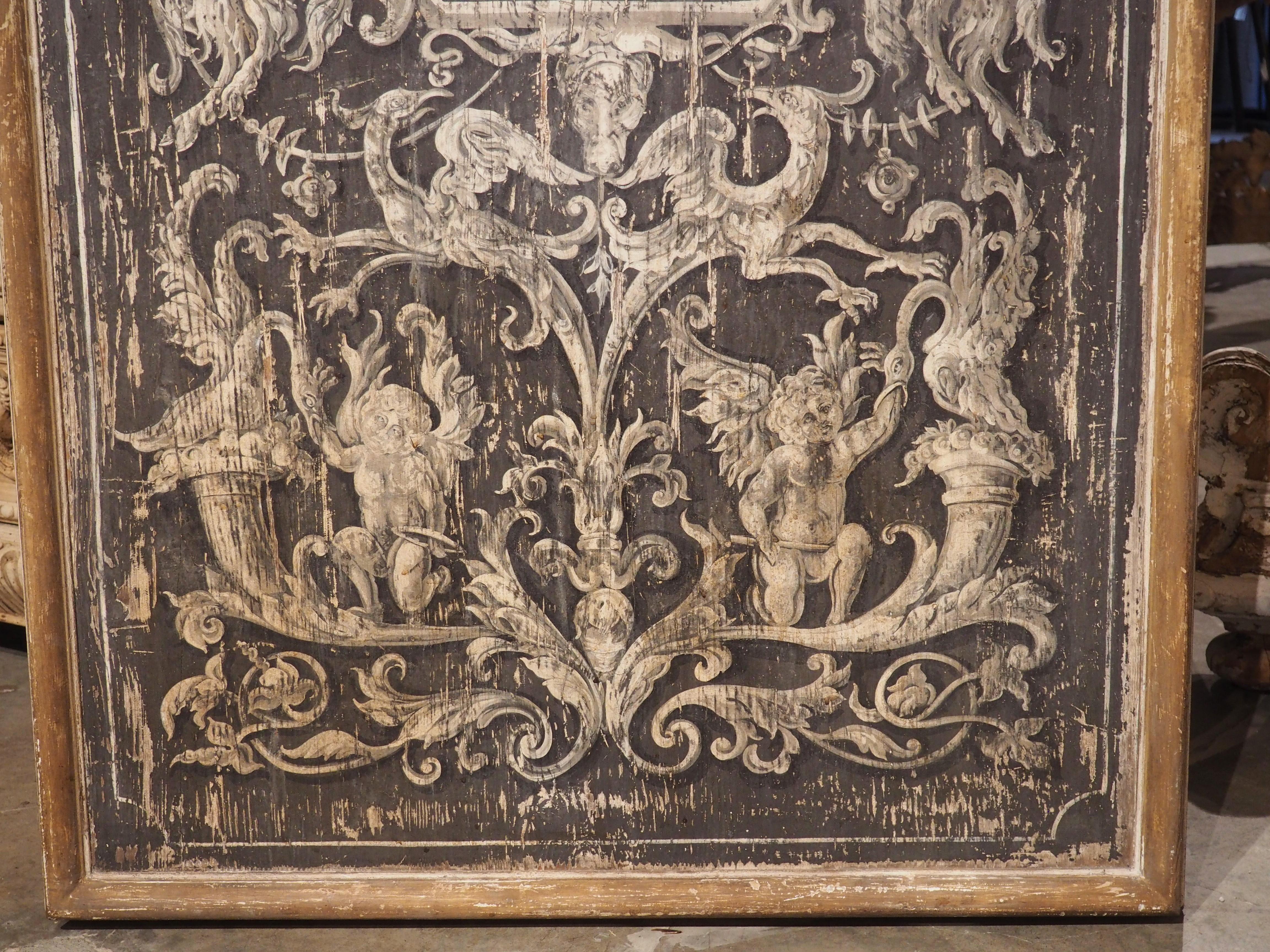 Hand-painted in Italy, this large, wooden wall panel features white and gray Neoclassical motifs over a black background. The images are surrounded by a thin white rectangular border with canted corners. A cavetto molding along the edge of the panel