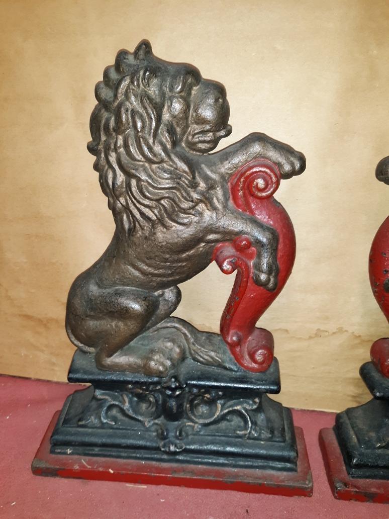 A handsome pair of cast iron Lion doorstops from the mid-19th century 1850-60. The lions are a mirror image of each other in a passant pose with a red painted scrolled columns resting on back plinth bases. Original paint with some expected wear.