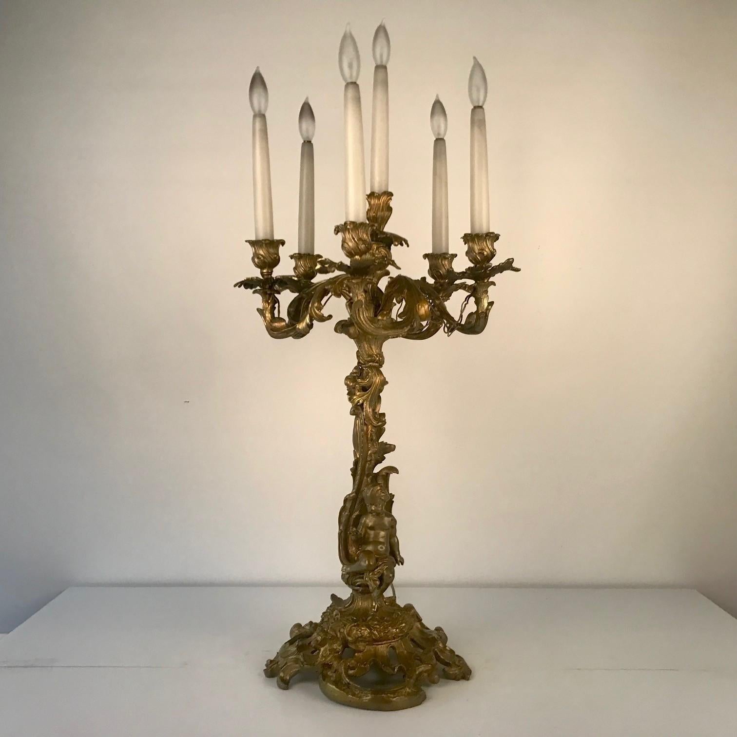 This is an especially sumptuous pair. Each base is pierced with stylised acanthus and en rocaille. The stems are modelled with putti in a leafy arbour and support five arms around a central light.

They are now surface wired for electricity.