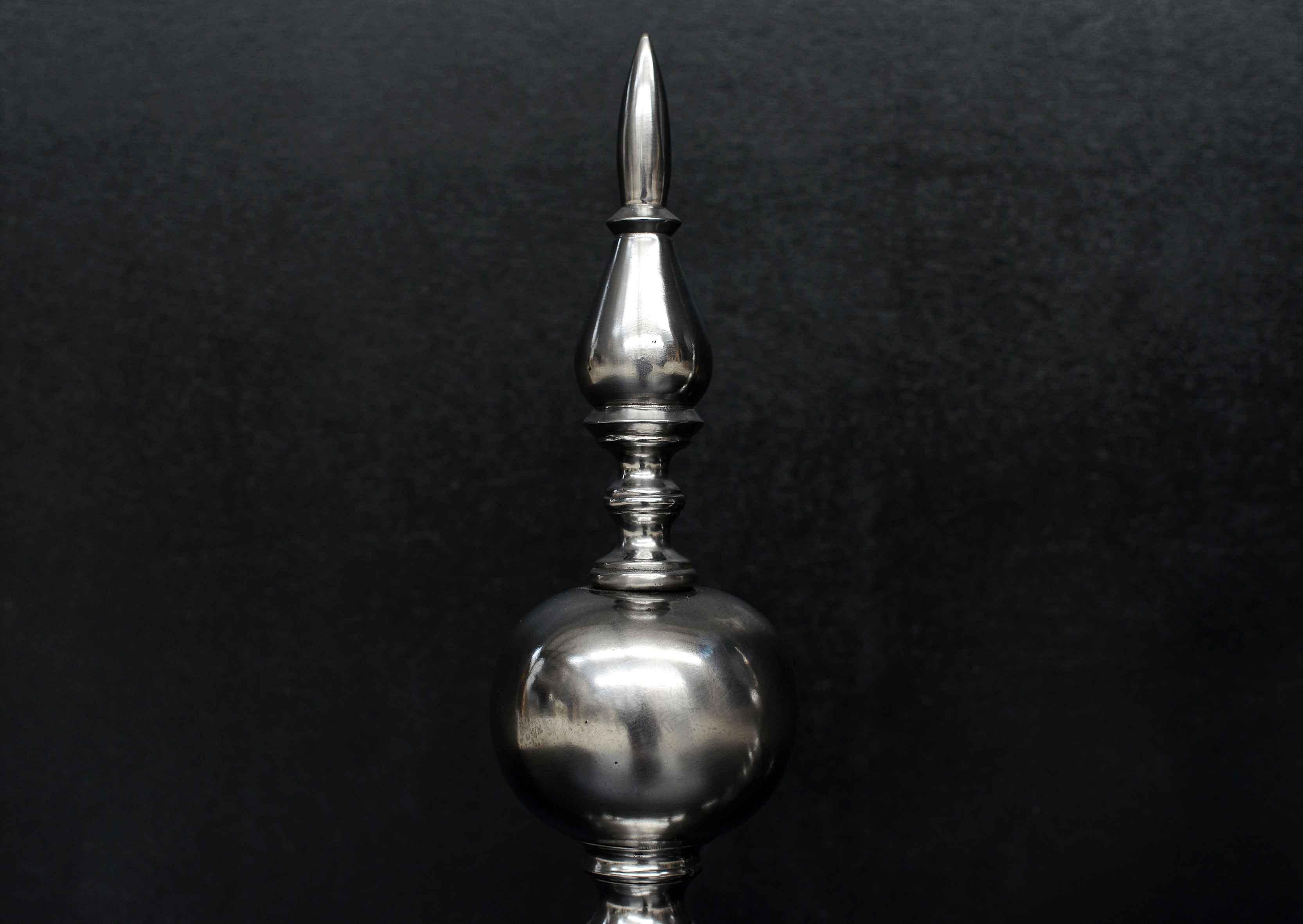 A substantial pair of polished steel firedogs. The horseshoe feet surmounted by ball and finial top. English, circa 1900. (Back bars could be amended to accept a log basket if required.)

Height:	615 mm       	24 ¼