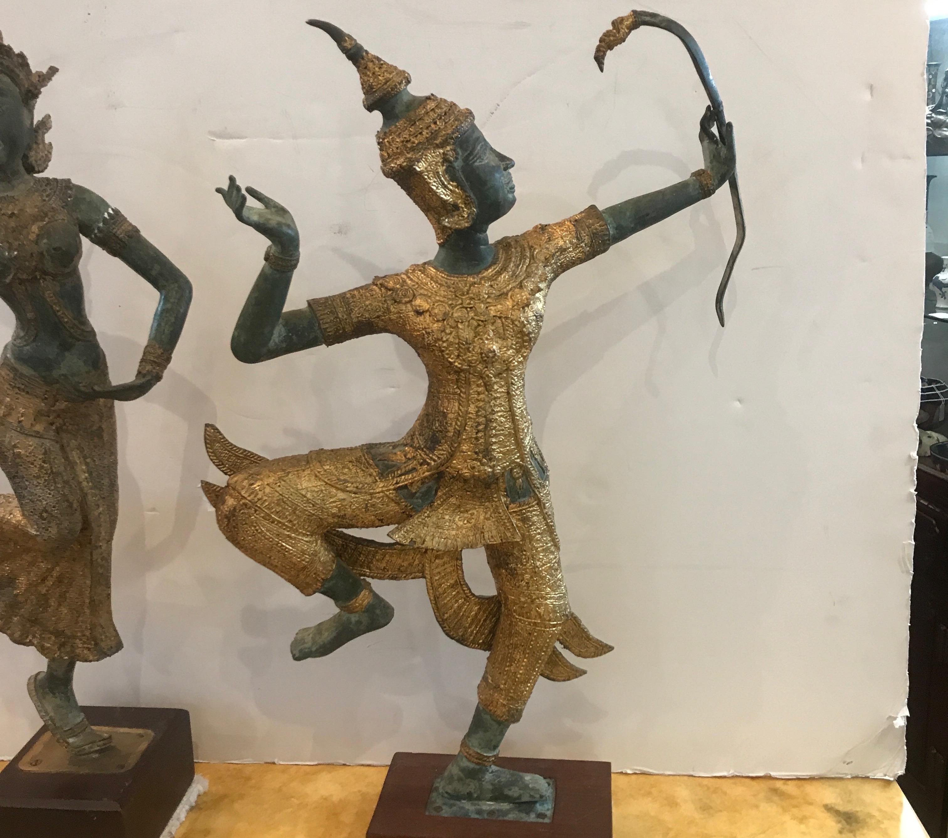 A pair of bronzed gilt and patinated Thai sculptures on hardwood bases. The exotic figures in an aged Verdi patination with the clothing in gold, early to mid 20th century. The highly figuratively posed figures one a female dance, the other a male