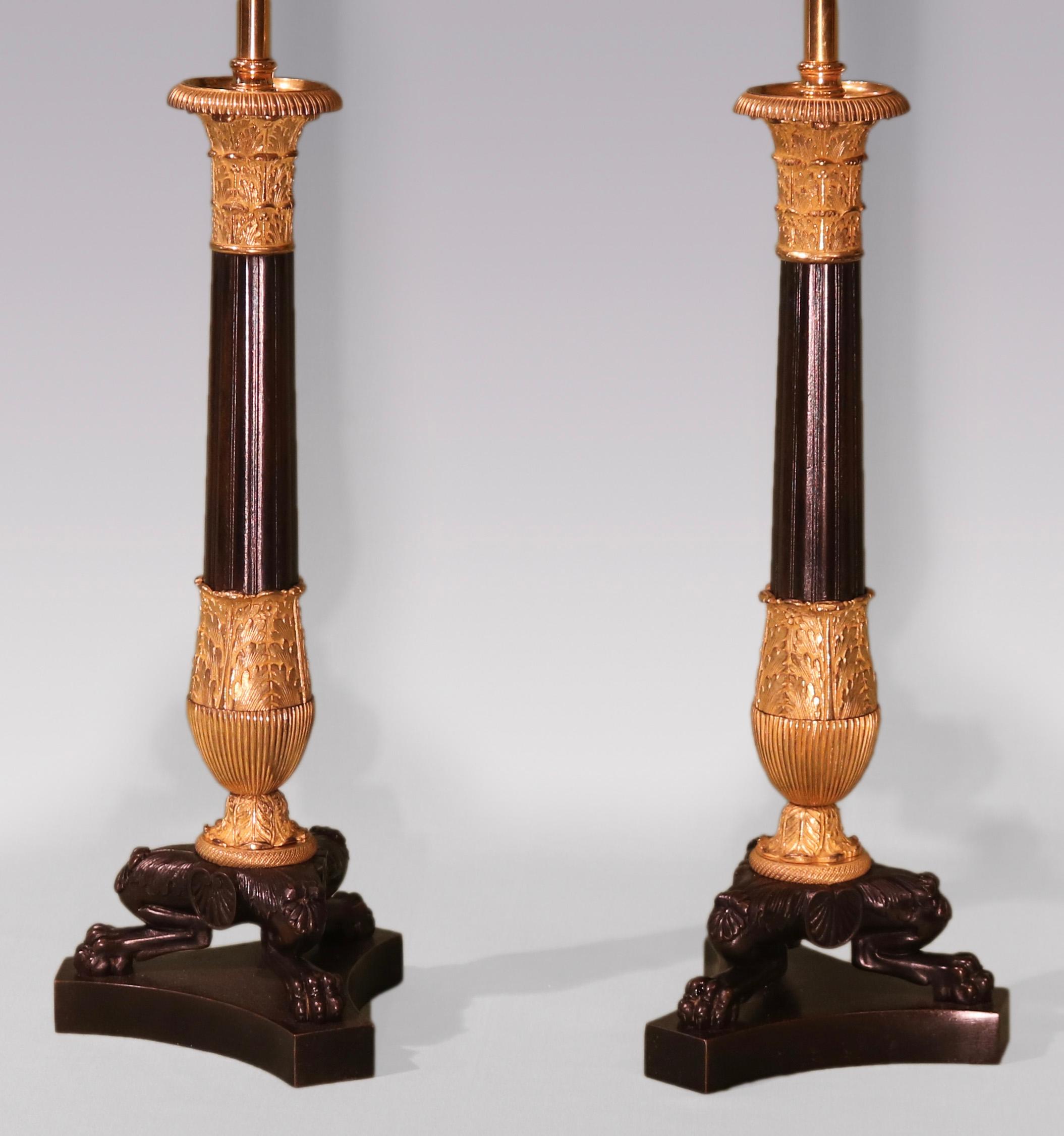 A large pair of early 19th century bronze & ormolu Candlesticks having “Corinthian Column” sconces above fluted stems with acanthus & reeded detail, supported on lion’ paw feet centred by scrolled medallions ending on triform platform bases.
