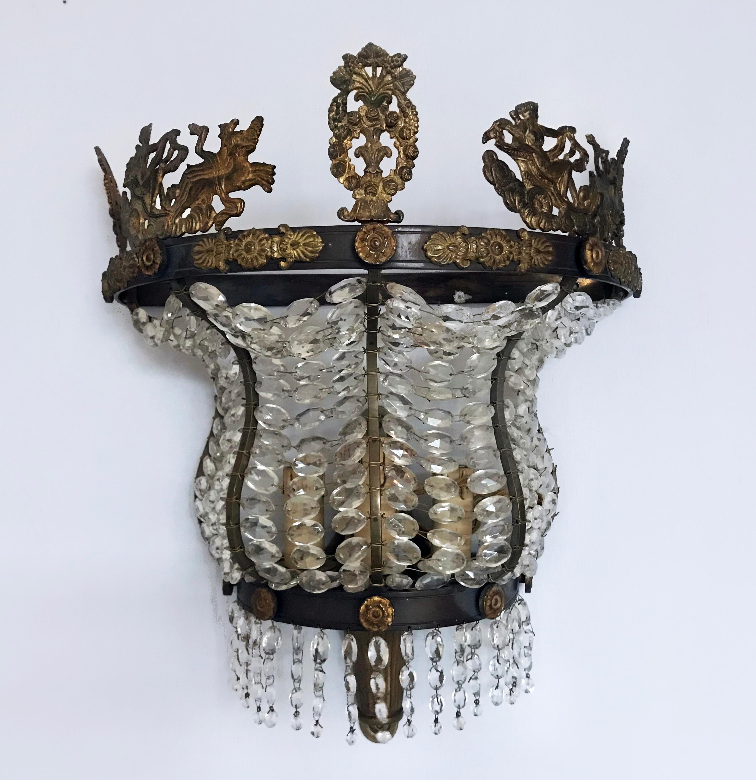 A highly unusual pair of French bronze-framed and ormolu-mounted Empire style wall lights. The well cast mounts depicting classical maidens in chariots centred by a floral garland with grapes. The whole enclosed with cut crystal beads.