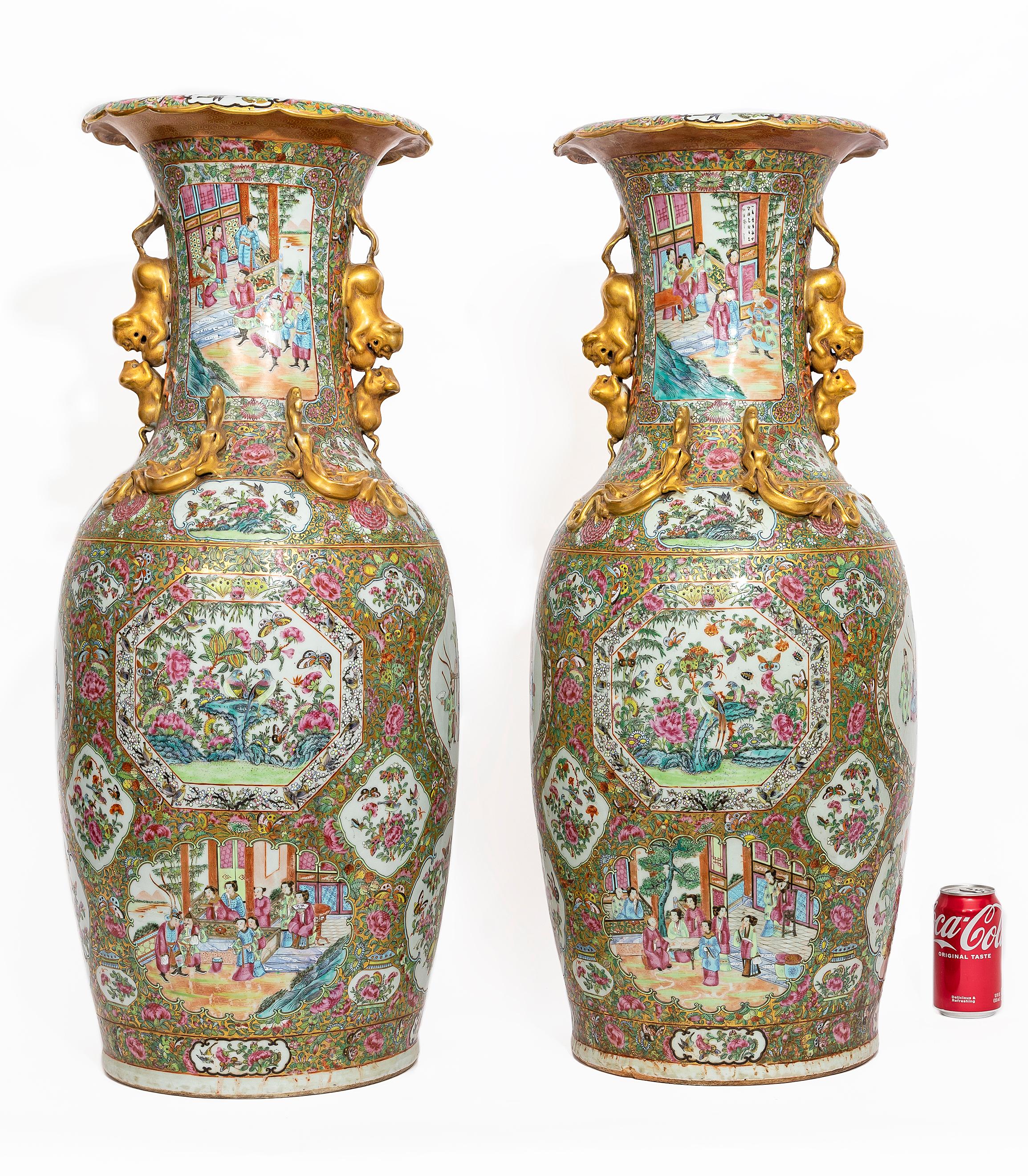A Large Pair of Chinese Famille Rose Decorated Gilt Foo Dog Handle Vases.  Each vase features finely painted scenes on cartouches.  The decoration showcases figures engaged in daily life and courtly activities, all set within intricately detailed
