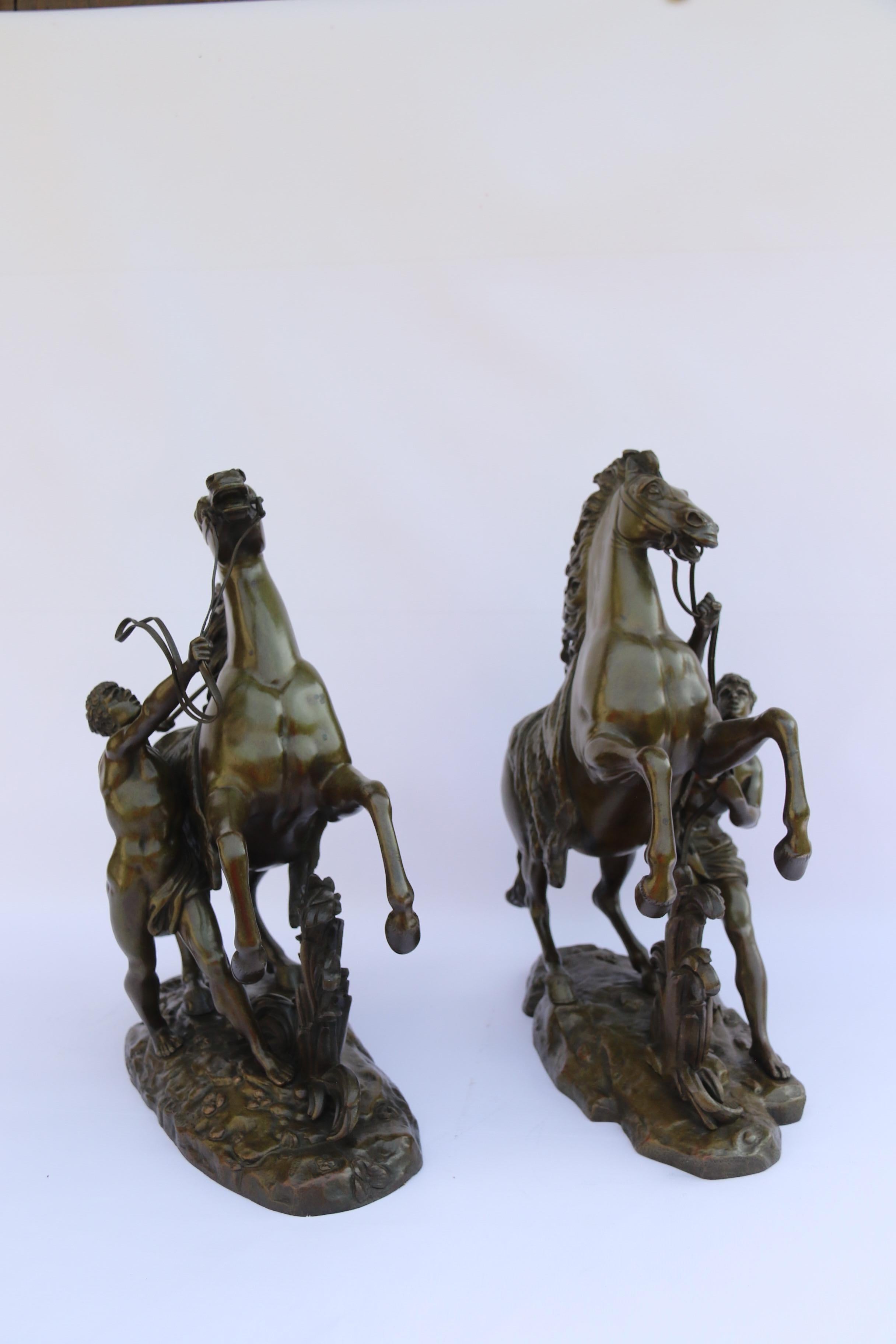This fantastic pair of 19th century finely sculpted, large scale bronze figures are after Guillaume Costou (1677 – 1746. )They each depict a wild prancing horse being restrained by the trainer who has them tethered on a short strap, and they capture