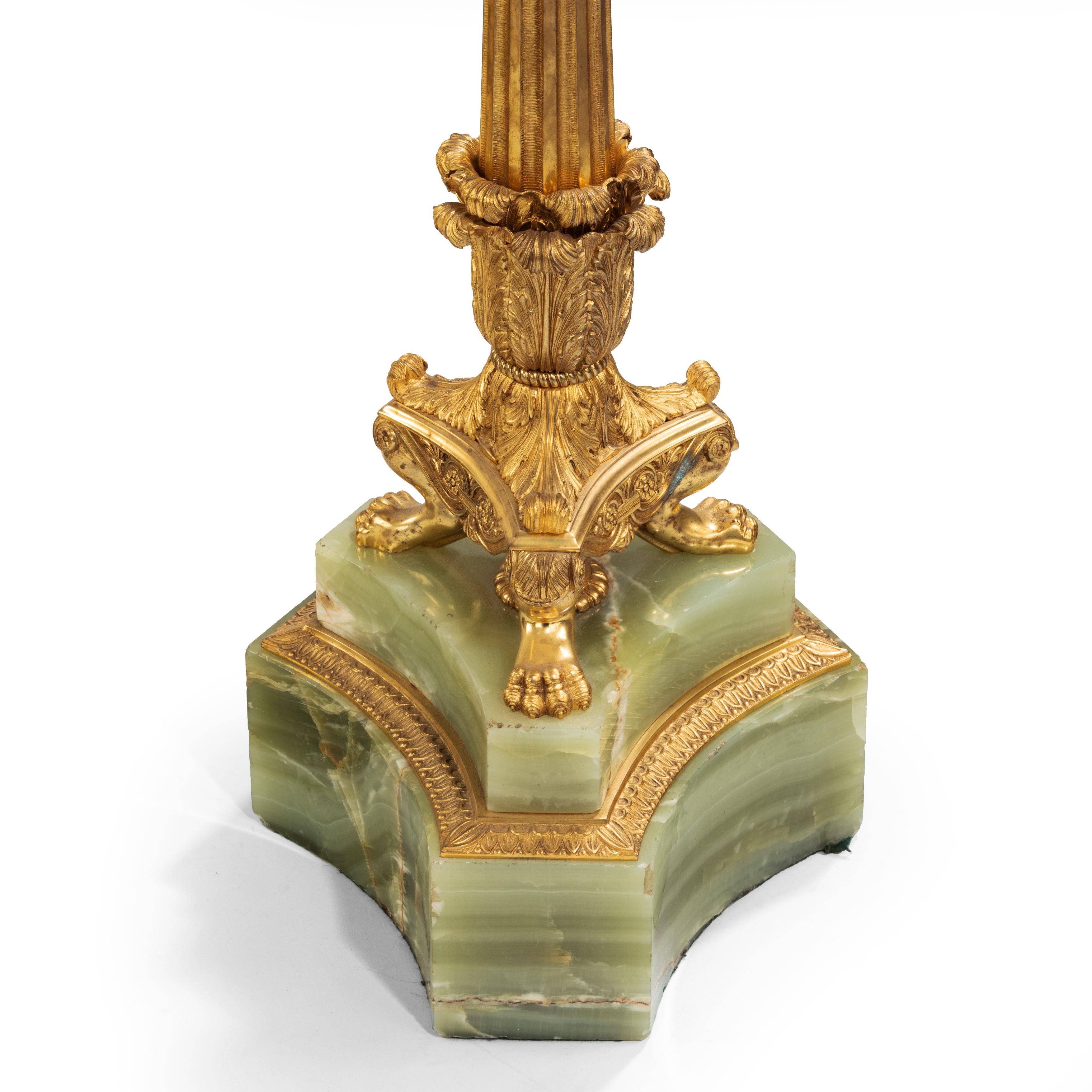 A large pair of onyx and ormolu lamps, each with a central fluted column surmounted by a sconce and supporting six further ornate branches of lights, all raised upon anthemion leaf collars set on tripod paw feet and triangular green onyx bases.