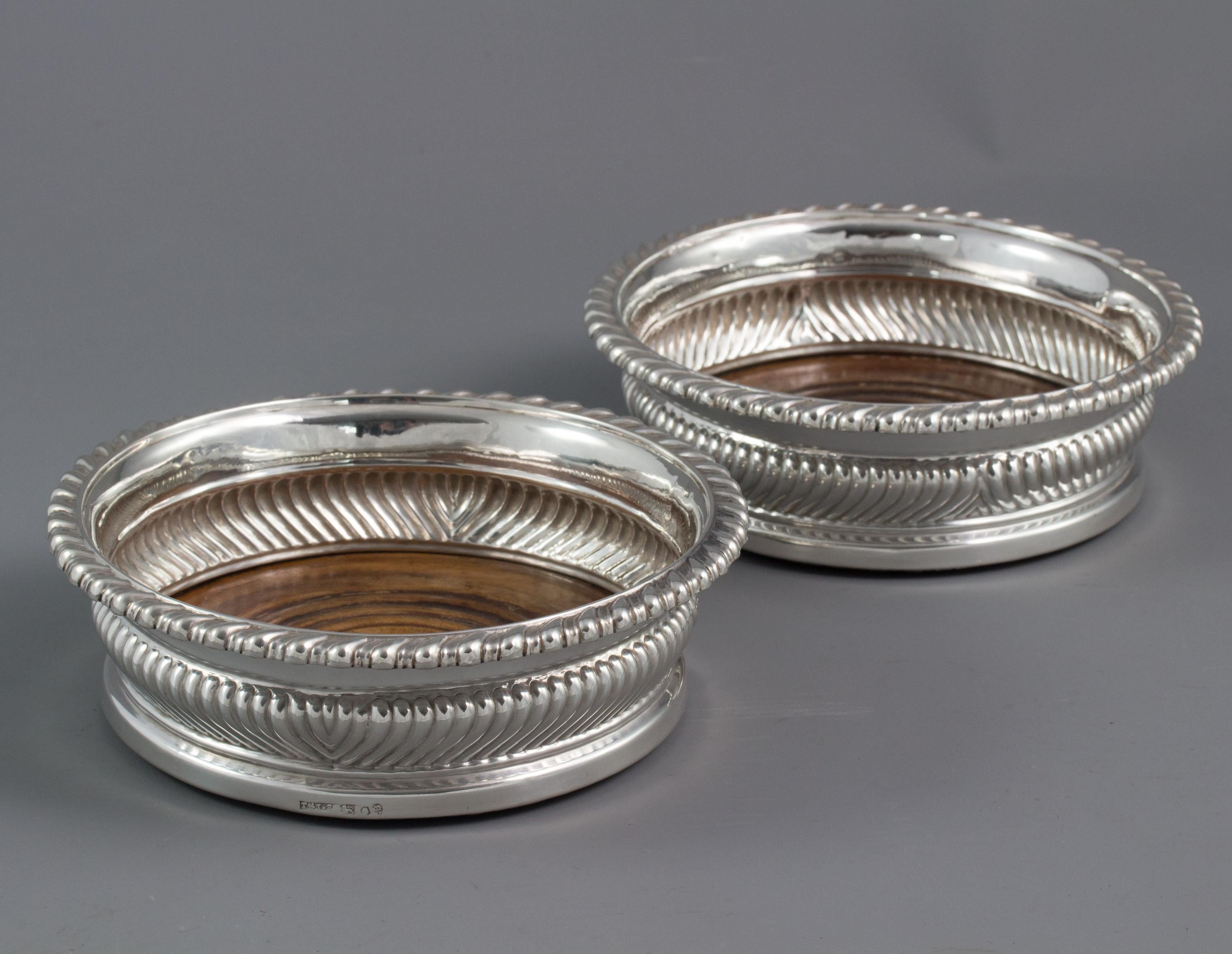 A very fine large pair of George III silver wine coasters, of circular form with half fluted shaped sides rising to a gadrooned rim. Turned wooden bases inset with a silver button engraved with a crest. The bases are lined with baize