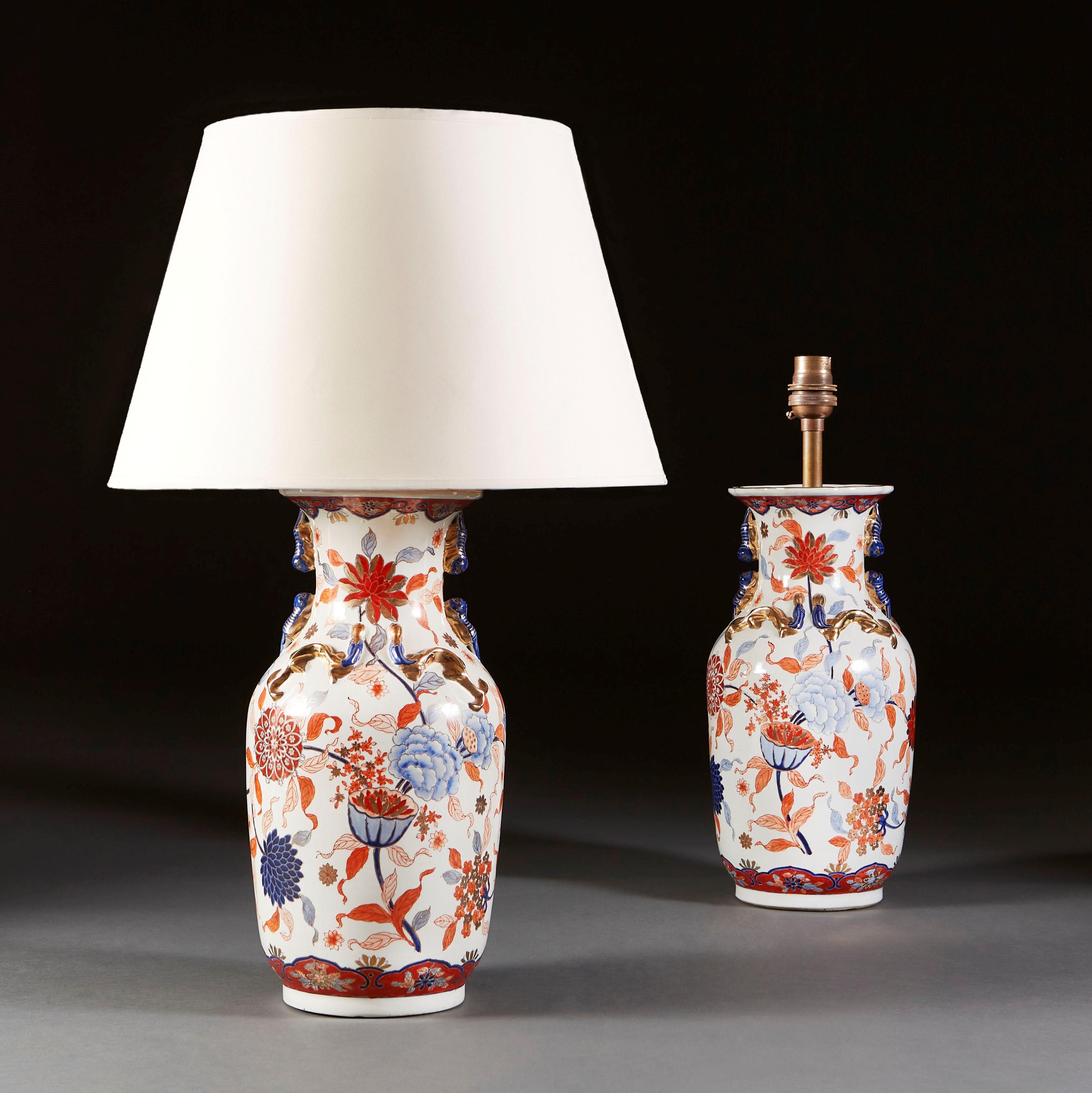 A large pair of late nineteenth century Japanese Imari vases, decorated throughout with tropical flora, with chrysanthemums and orchids in red and blue glaze on a white ground, the necks with dragon handles and scrolls, now as lamps.

Currently