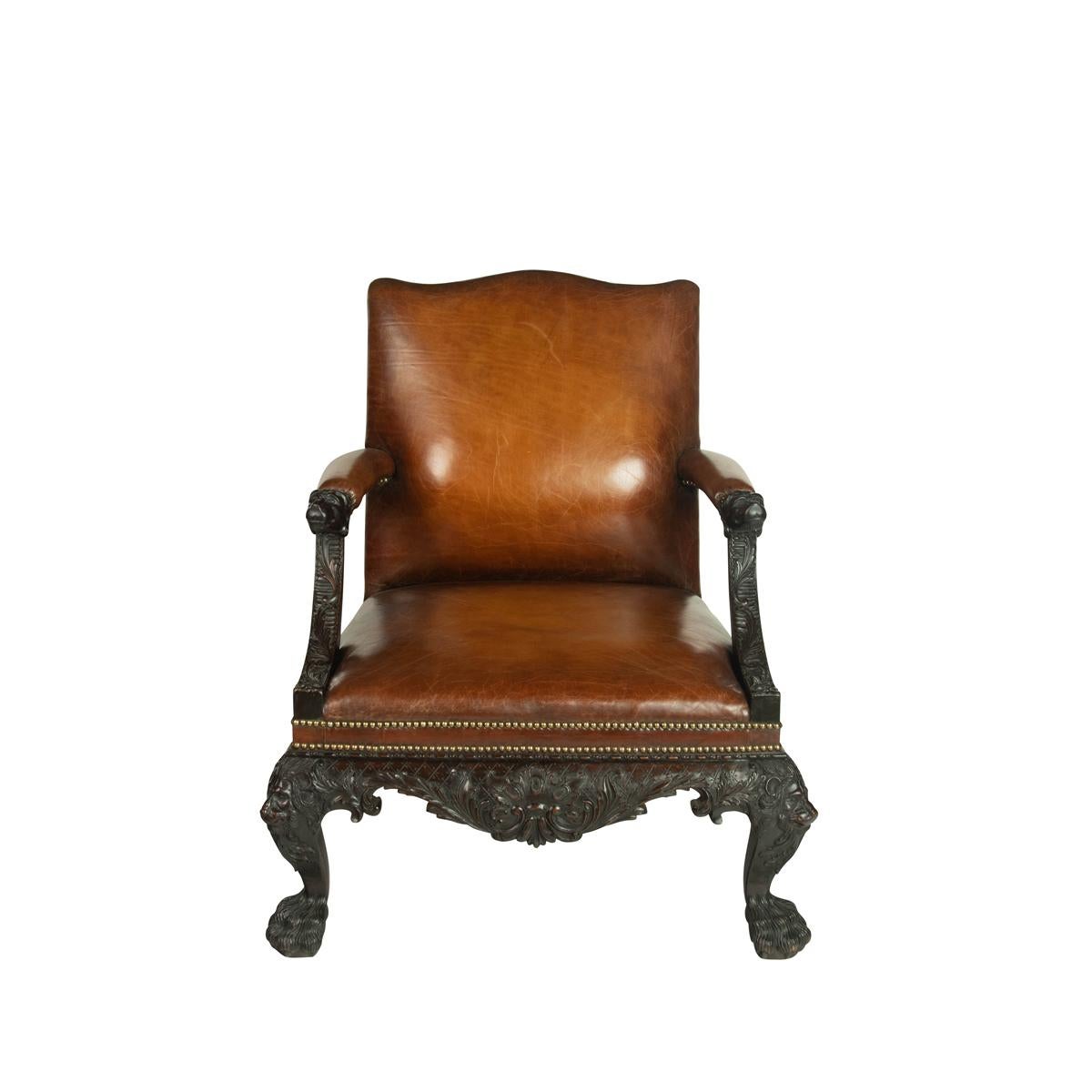 A large pair of Irish mahogany  library armchairs in the  Georgian style , each with the shaped rectangular back, arm rests and seat upholstered in chestnut leather with close studded brass nails, richly carved with lions’ heads to the arms and