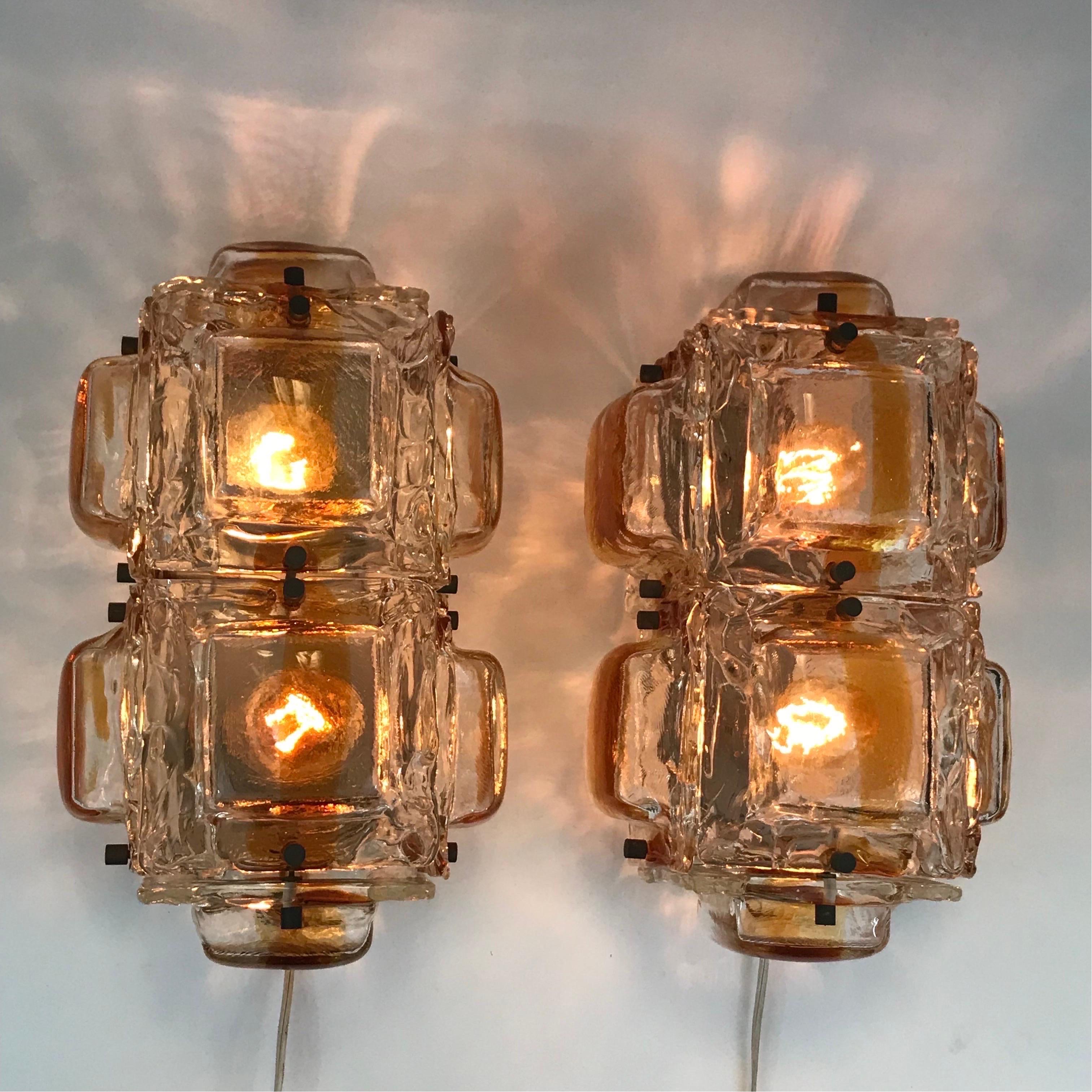 A large pair of rectangular Mazzega sconces comprised of a metal frame housing two bulbs and supporting the armature to encase the lights in eight thick fused glass square shades in clear crystal color with an amber stripe in each. In overall