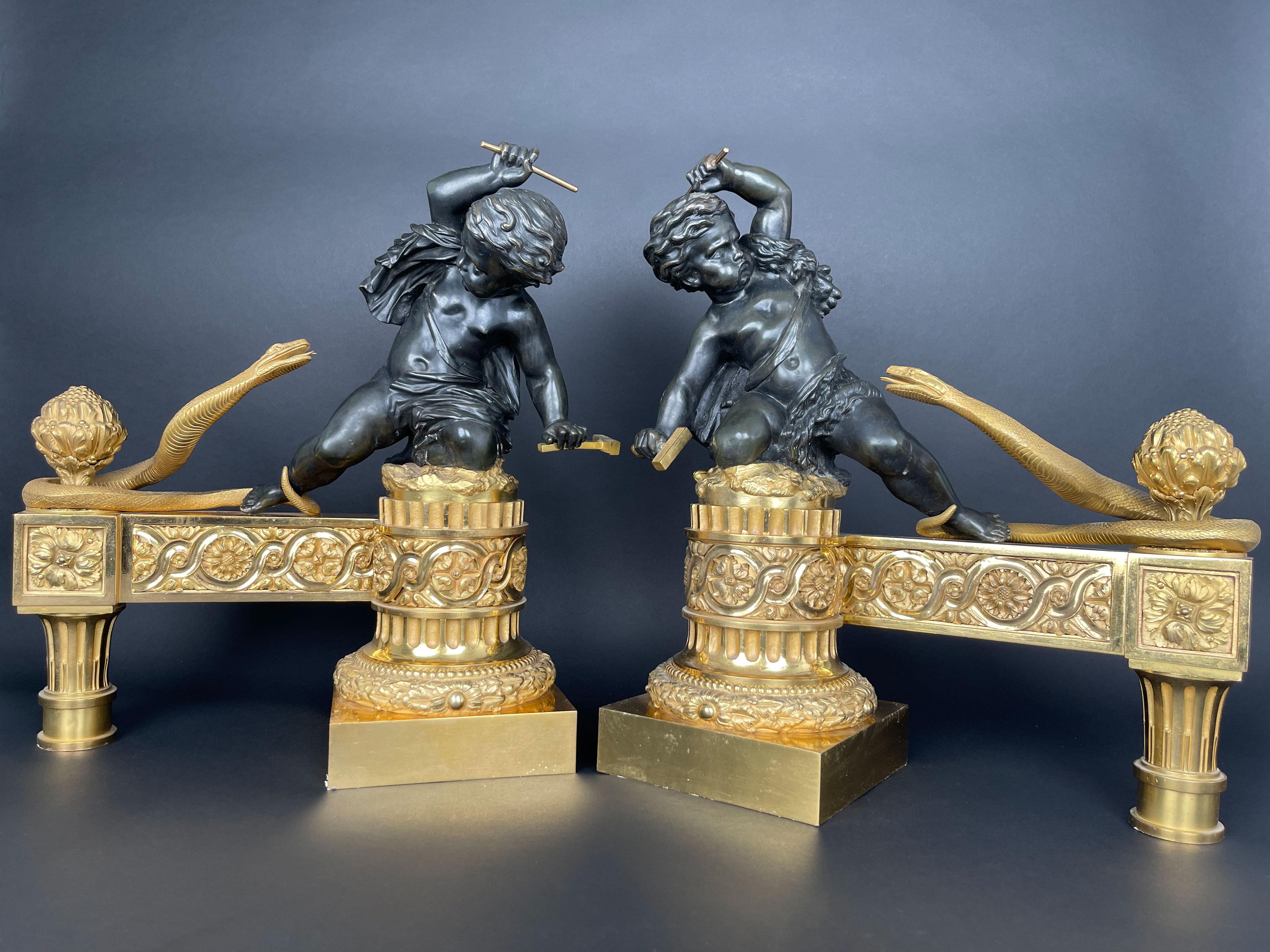 A Large And Very Heavy Pair Of Gilt & Patinated Bronze Chenets By Henry Dasson. Two patinated bronze cupids seating on top of columns with raised hands holding a weapon fighting attacking snakes. 

 France, Circa