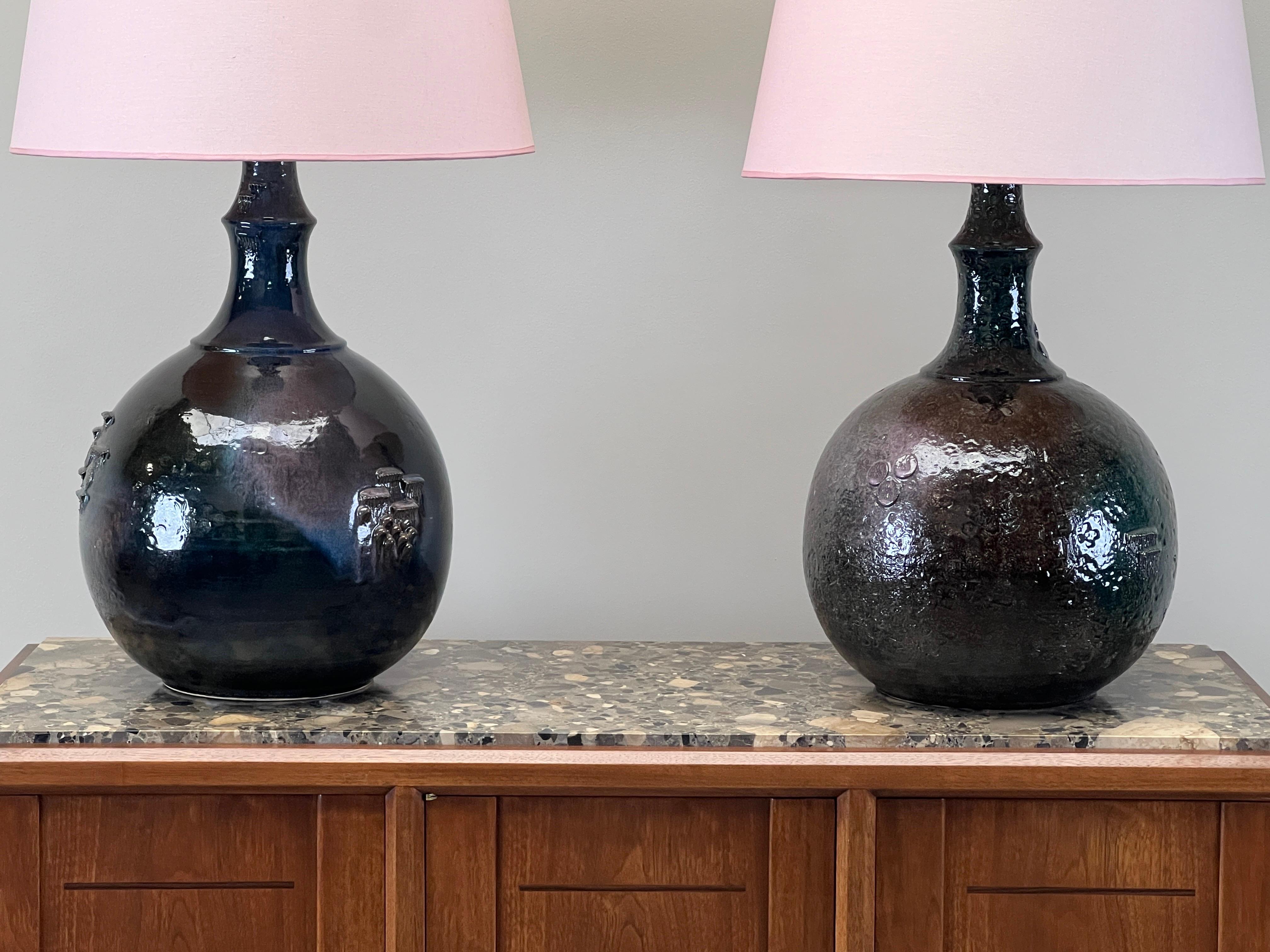 A large pair of hand made ceramic lamps by Bjorn Wiinblad. Each lamp is unique with varied texture and coloration. A beautiful and subtle array of pinks and blues come through the glaze when seen in person. Original pink shades and wiring. 