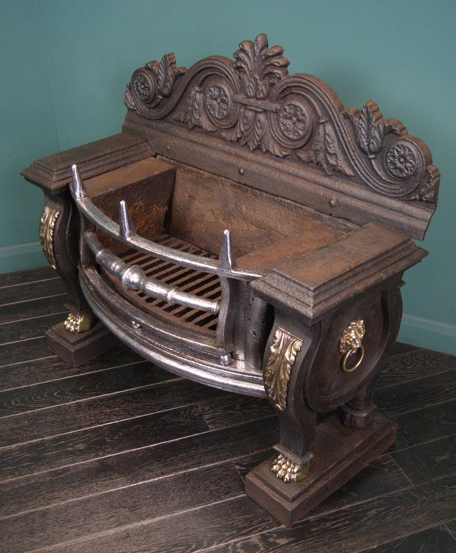 An imposing Regency sarcophagus fire grate with a polished wrought bow-front, comprising of obelisk log stops, swept semi-circular hob fronts with conforming fret, turned centre bar and ball detail. Cast-iron structure adorned with brass paw-feet,