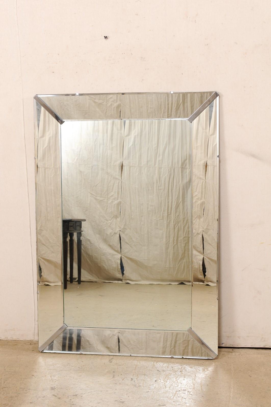 A vintage American larger-sized mirror within a clear glass frame. This rectangular shaped mirror stands just shy of five feet tall and 41 inches wide. It features a clear center glass center within a thick surround of mirrored glass, and