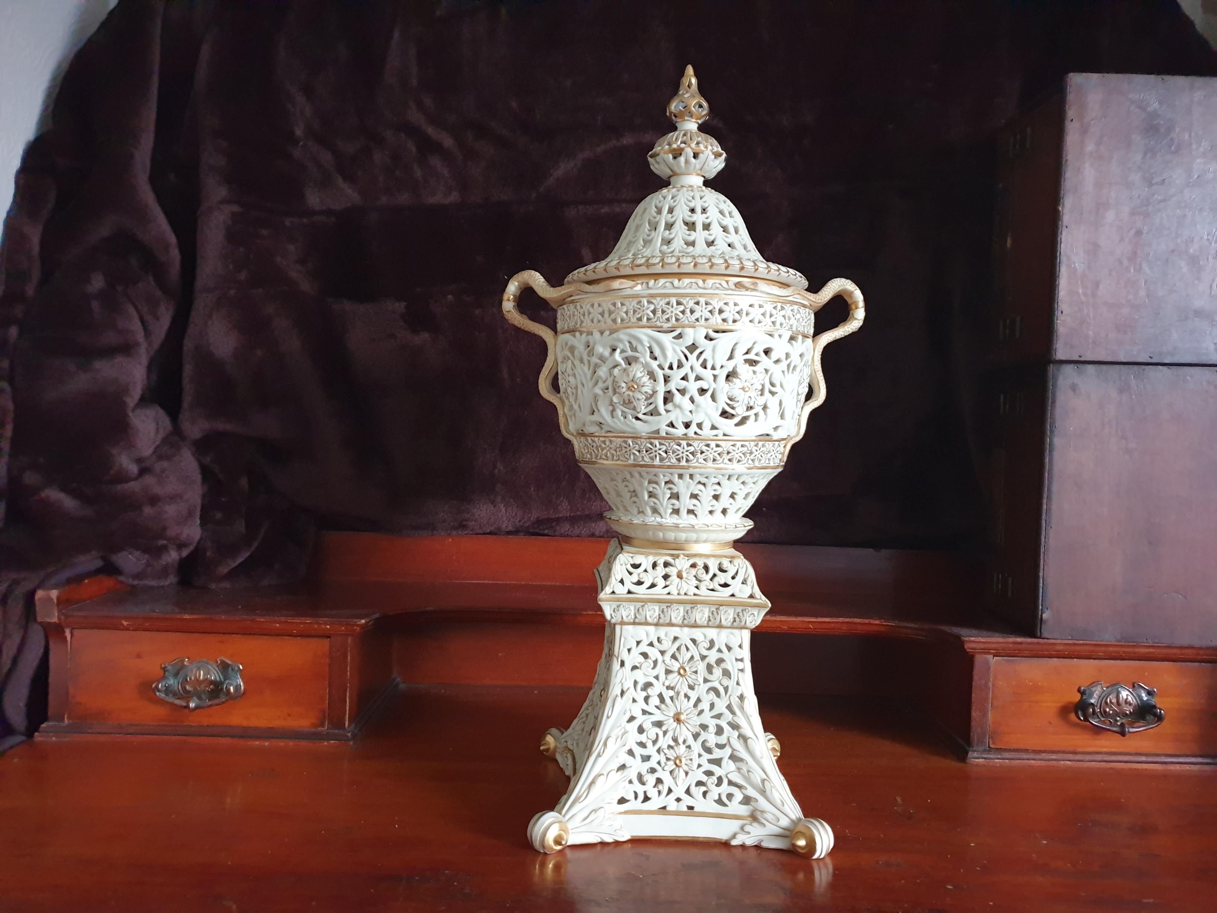 A late 19th century Grainger & Co, Worcester large reticulated pot pourri vase and cover,the urn-shaped vase pierced and gilded with scrolling foliate with forked serpent handles, raised on a tapering square plinth, the domed cover with pierced and