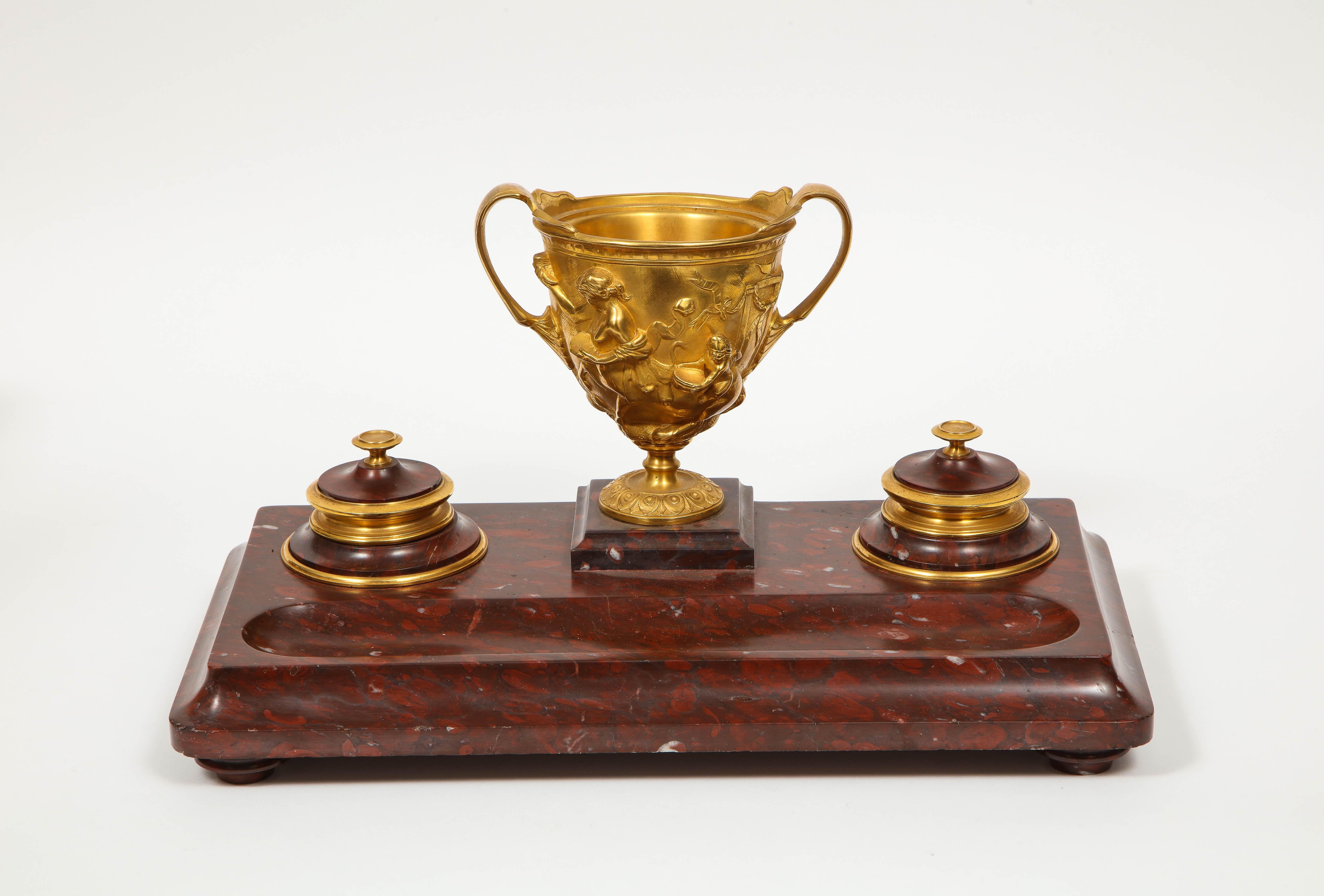 A large rouge marble and gilt bronze inkwell Encrier, attributed to Barbedienne.

Of rectangular form, nice thick rouge marble slate, with gilt bronze mounts and central vase, circa 1890.

Very good condition, missing glass inserts.