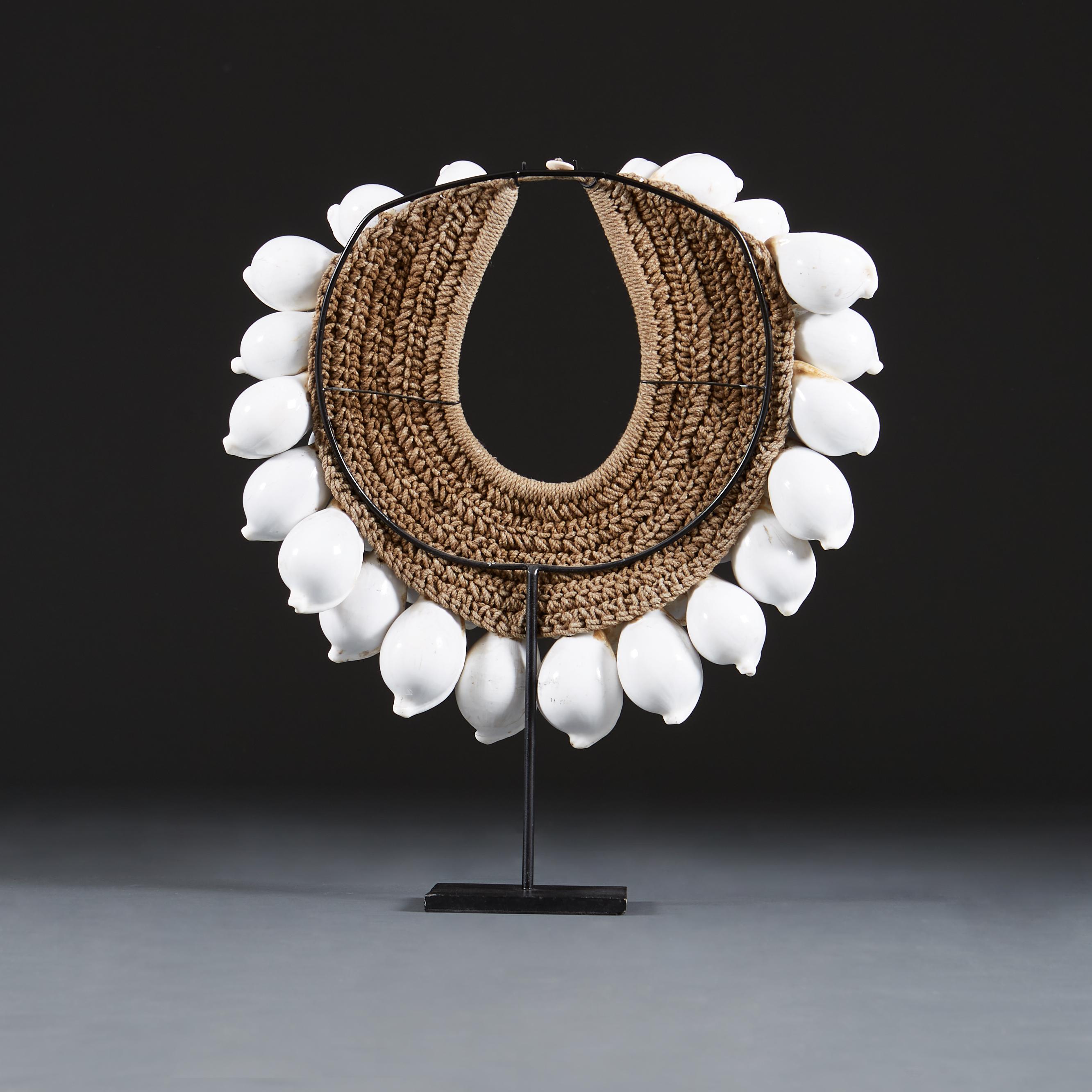 A rare early 20th century cowrie shell necklace made with unusually large and brilliant white cowrie shells, all the shells equally sized throughout, backed on a woven abaca ground, with bespoke metal display stand. Can also be worn as a necklace.