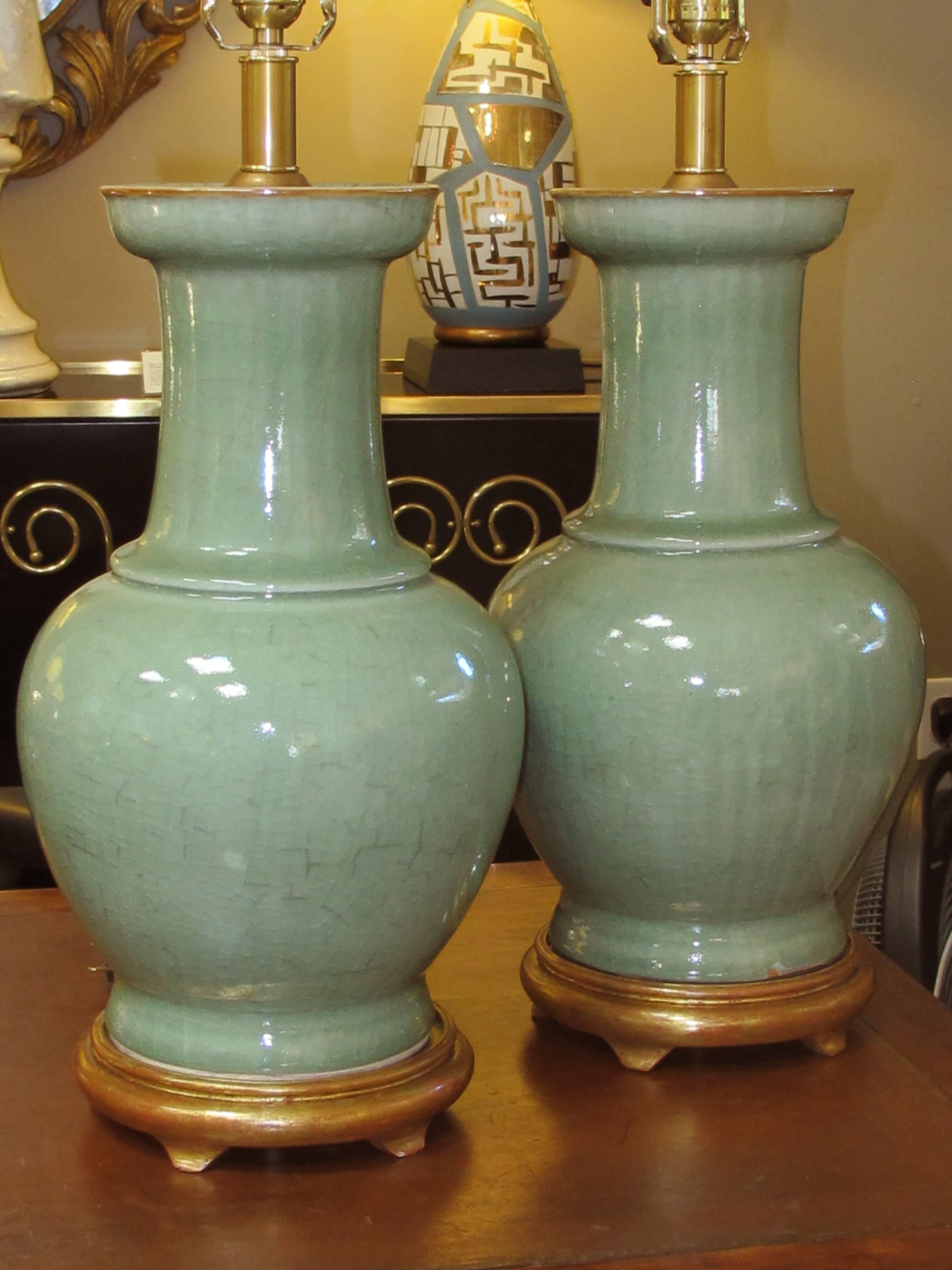 These classic lamps each with impressive size with a lovely celadon glaze all raised on a gilt-wood base; with fine overall craquelure and wear with ash glaze remnants.