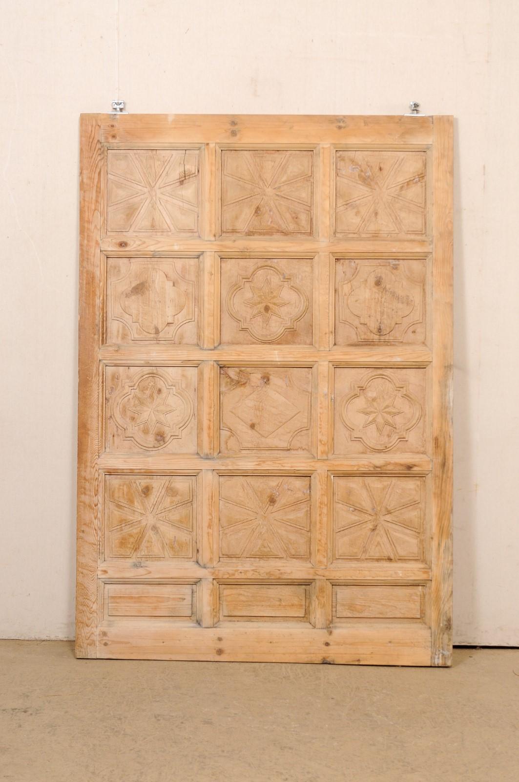 A Spanish large-size, decoratively-carved, raised-panel wooden door. This vintage wood door from Spain is adorn with 15 raised panels, with three rows of panels across and five down. Each of the four top rows have a squared-shape with embellished