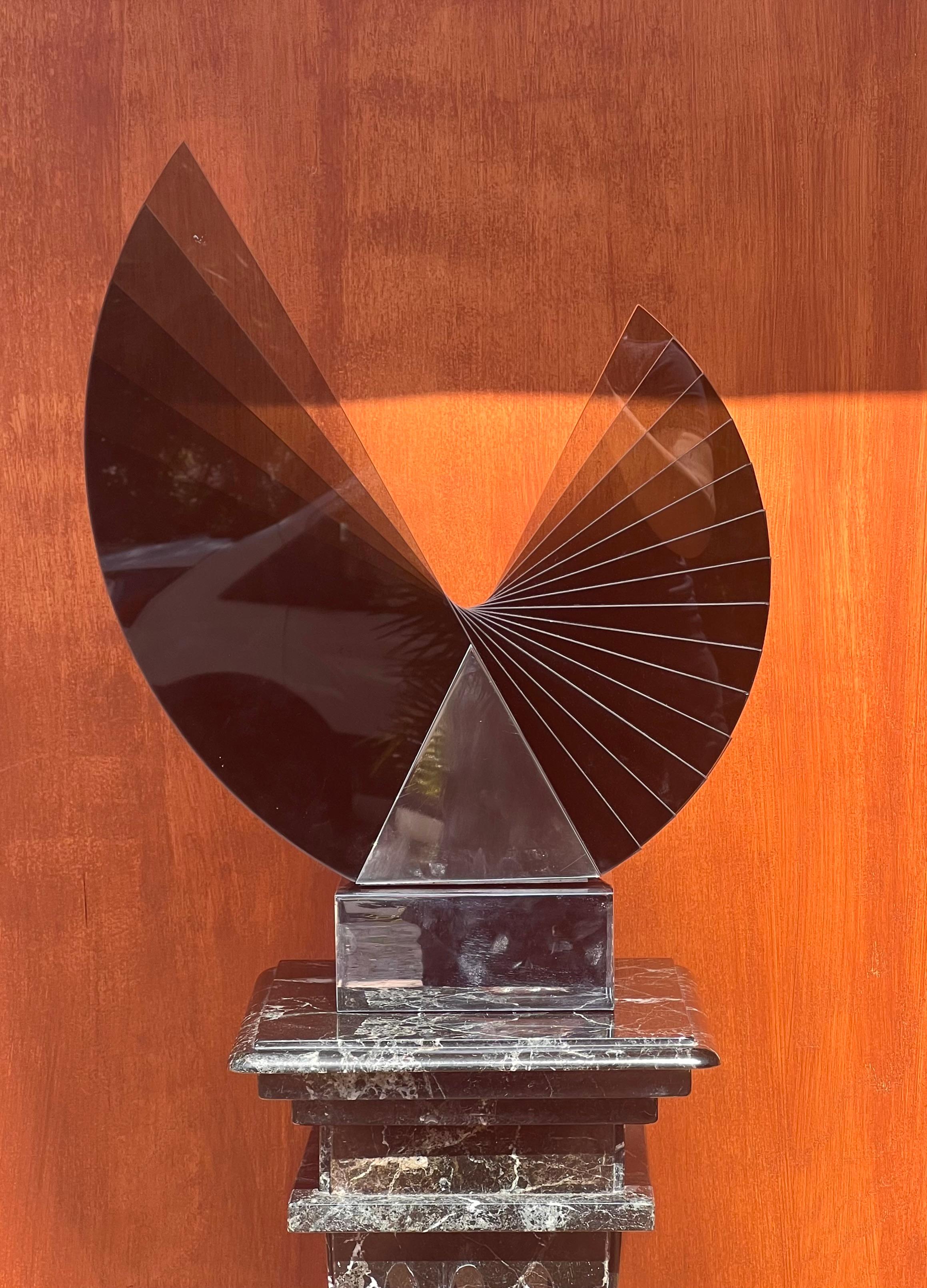 A stunning smoked glass and metal sculpture by Runstadler Studios, signed, 1990. Edition 20/30, this rare piece depicts periods a large wing fanning out, emerging from a chrome plinth. The wing spins manually on its plinth, when urged, should the