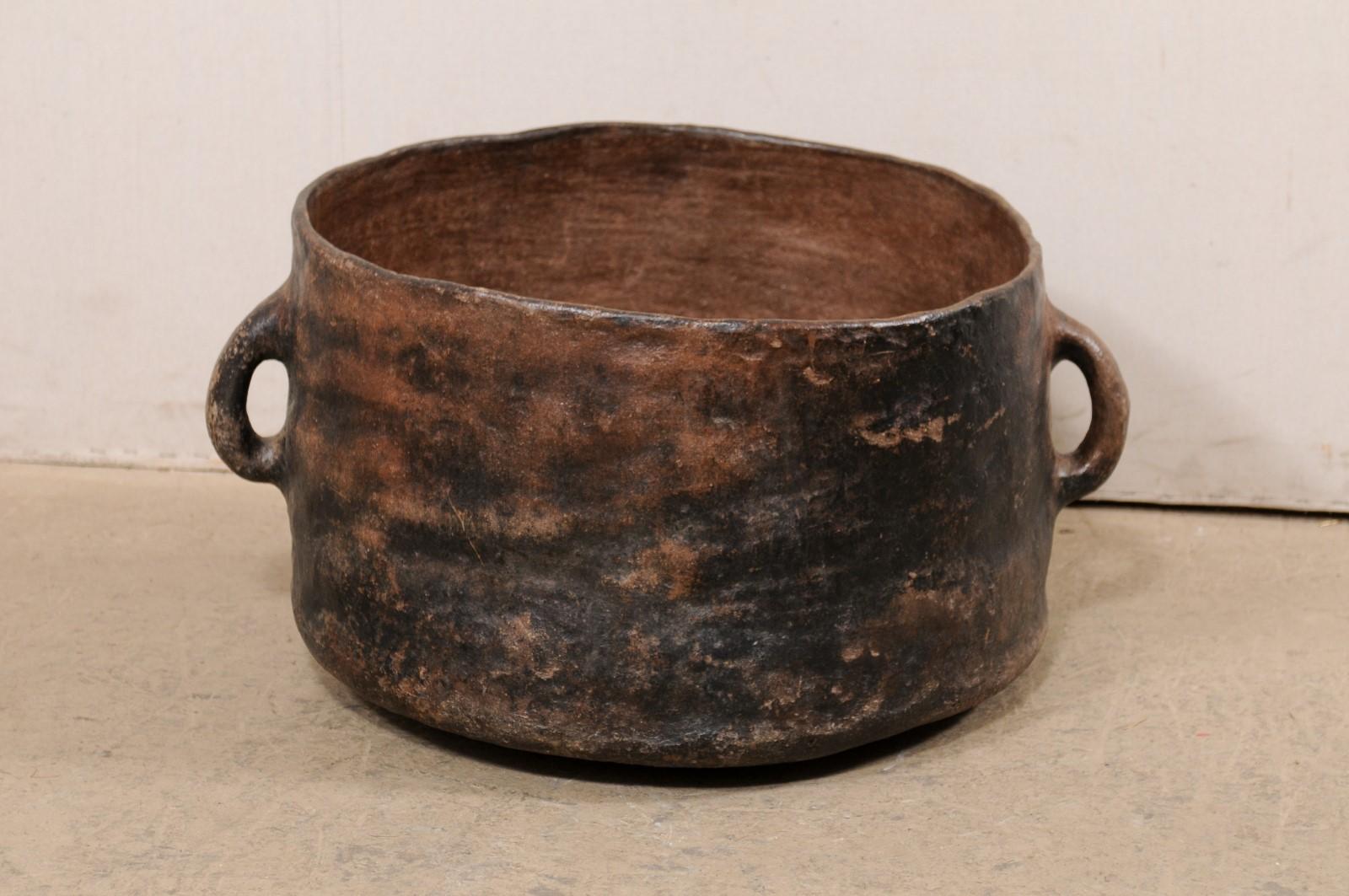 A Spanish Colonial cooking pot from the early 20th century, Central America. This antique cooking vessel has been made of clay, is round-shaped and flanked by a pair of handles at each far side. This pot is perfectly-imperfect, with hand sculpted