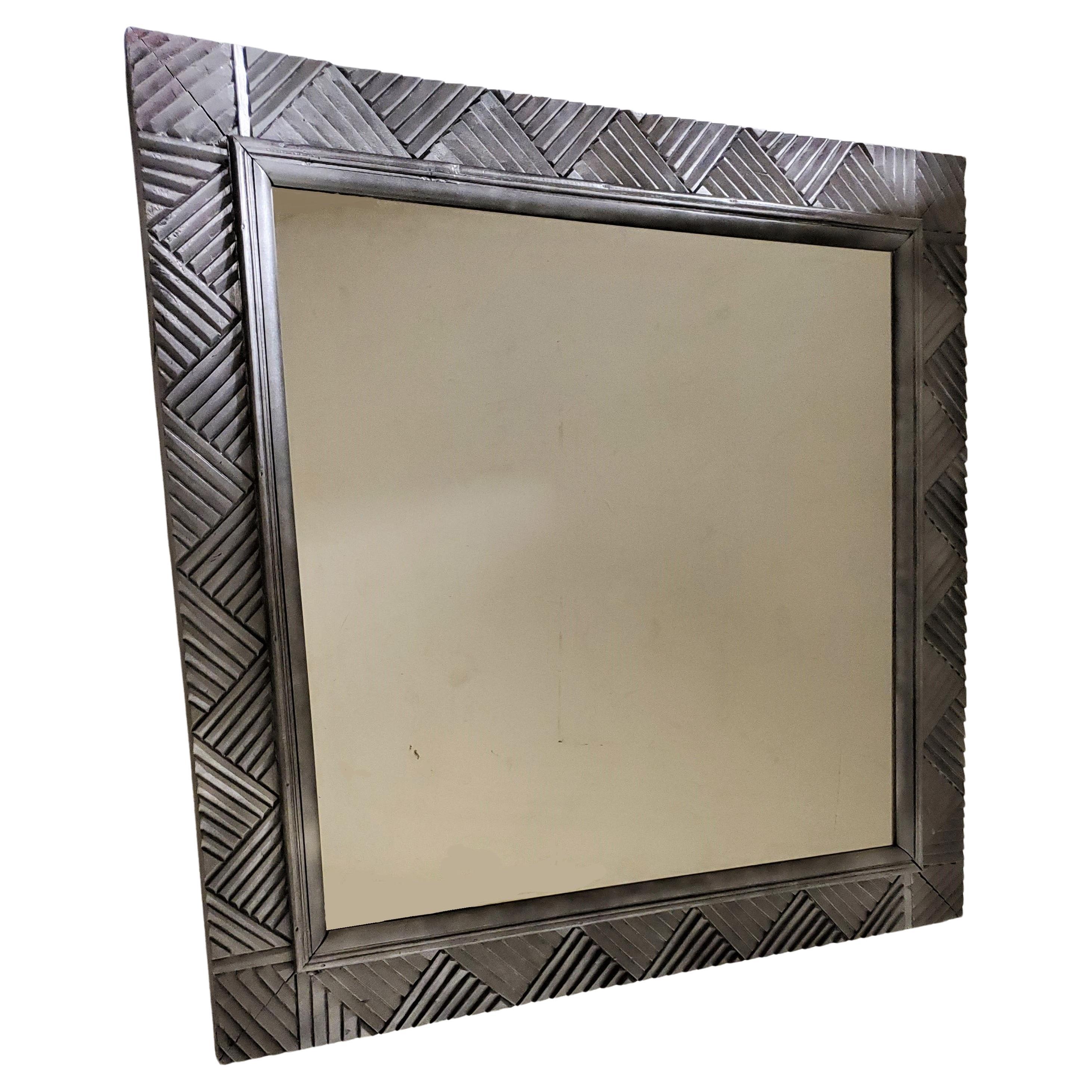 An impressive and decorative carved wood wall mirror of overall geometric motif. 
Square shape with a satin silvered finish and 3-D textured effect with triangular, chevron, stepped patterns.
The perfect size for over a fireplace mantle, in a