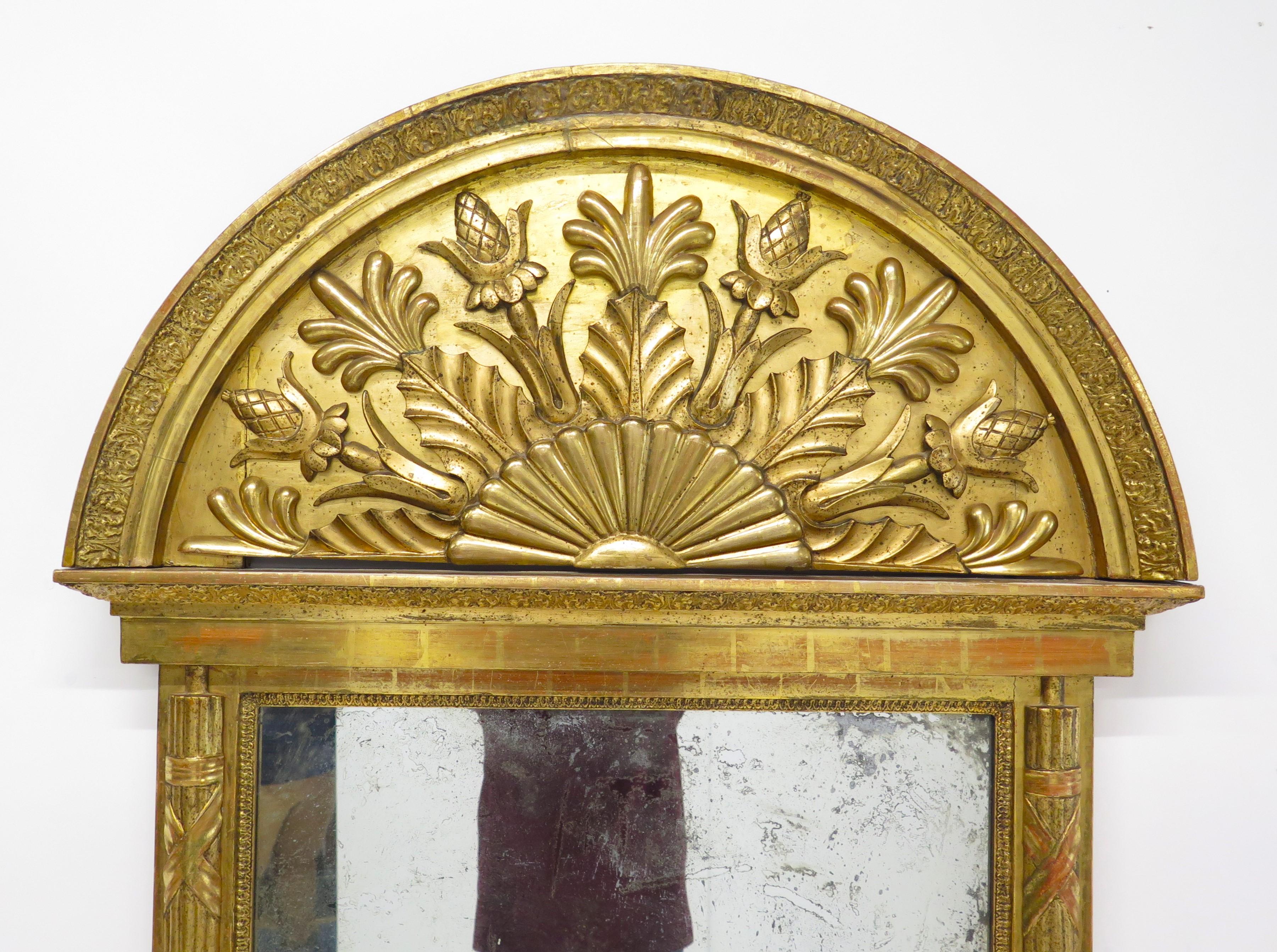 Gran espejo de muelle neoclásico sueco de madera dorada, el espejo presenta una cresta arqueada y medias columnas estriadas flanqueantes, dentro del arco hay una decoración que recuerda a una flor o a un rayo de sol con follaje alrededor, adornando