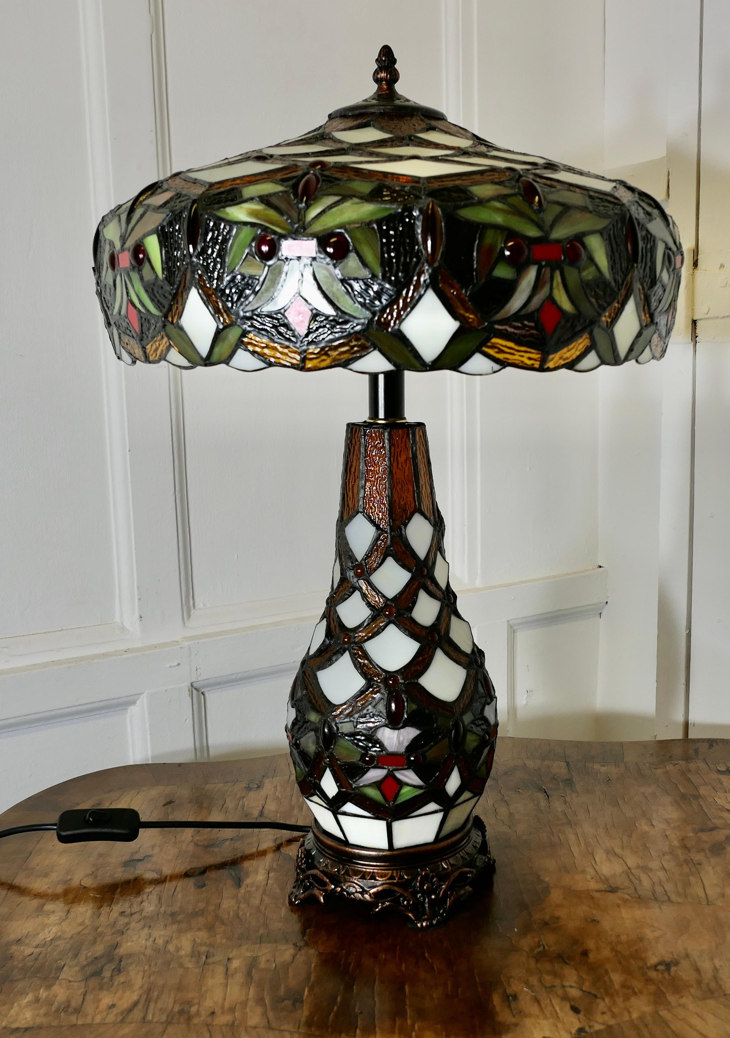 A Large Tiffany Style Stained Glass Table Lamp and Shade

A very unusual and stunning piece, the lamp and the shade are made in  leaded and jewelled glass, the base of the lamp has a lightbulb inside to show the superb design which is repeated in