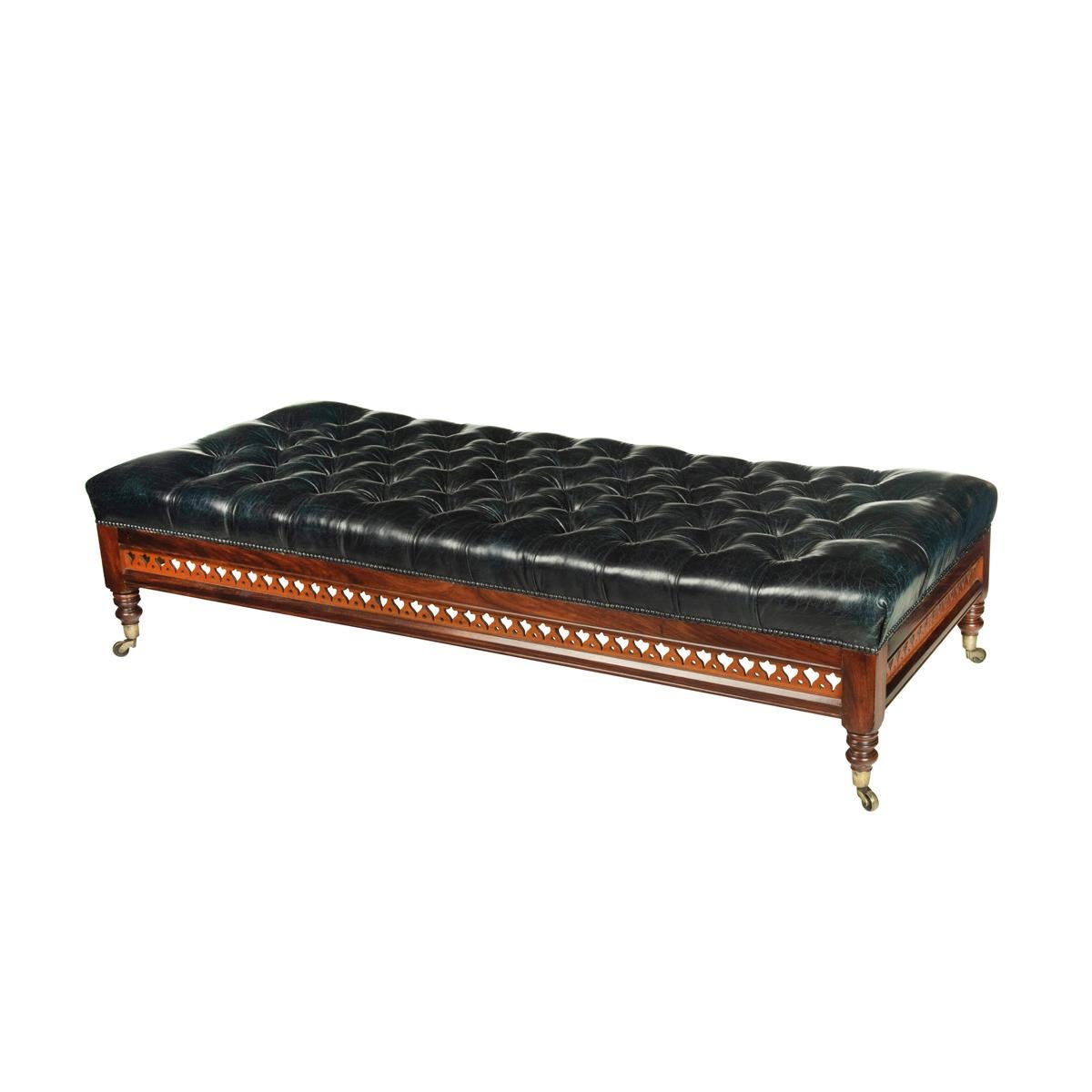 A large Victorian leather stool, of long rectangular form, the deep buttoned top reupholstered in blue-black leather, the frieze pierced with a band of flower-buds, all raised on turned legs with the original castors, a maker’s label underneath