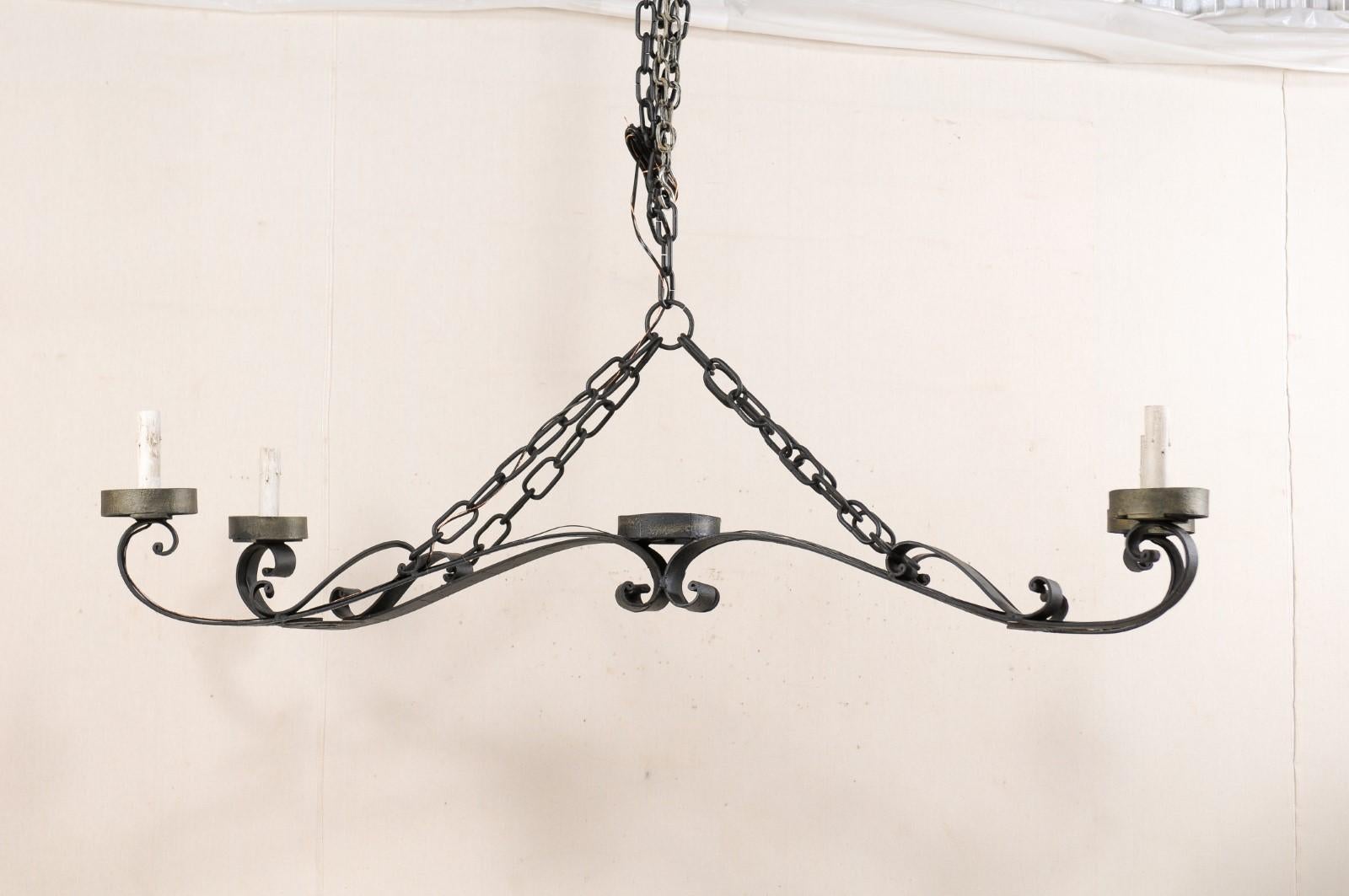 A large-sized French black iron chandelier from the mid-20th century. This vintage chandelier from France, with it's expansive spread of over 5 feet in width, has a light and airy feel with four elongated s-shaped arms which connect in the center,