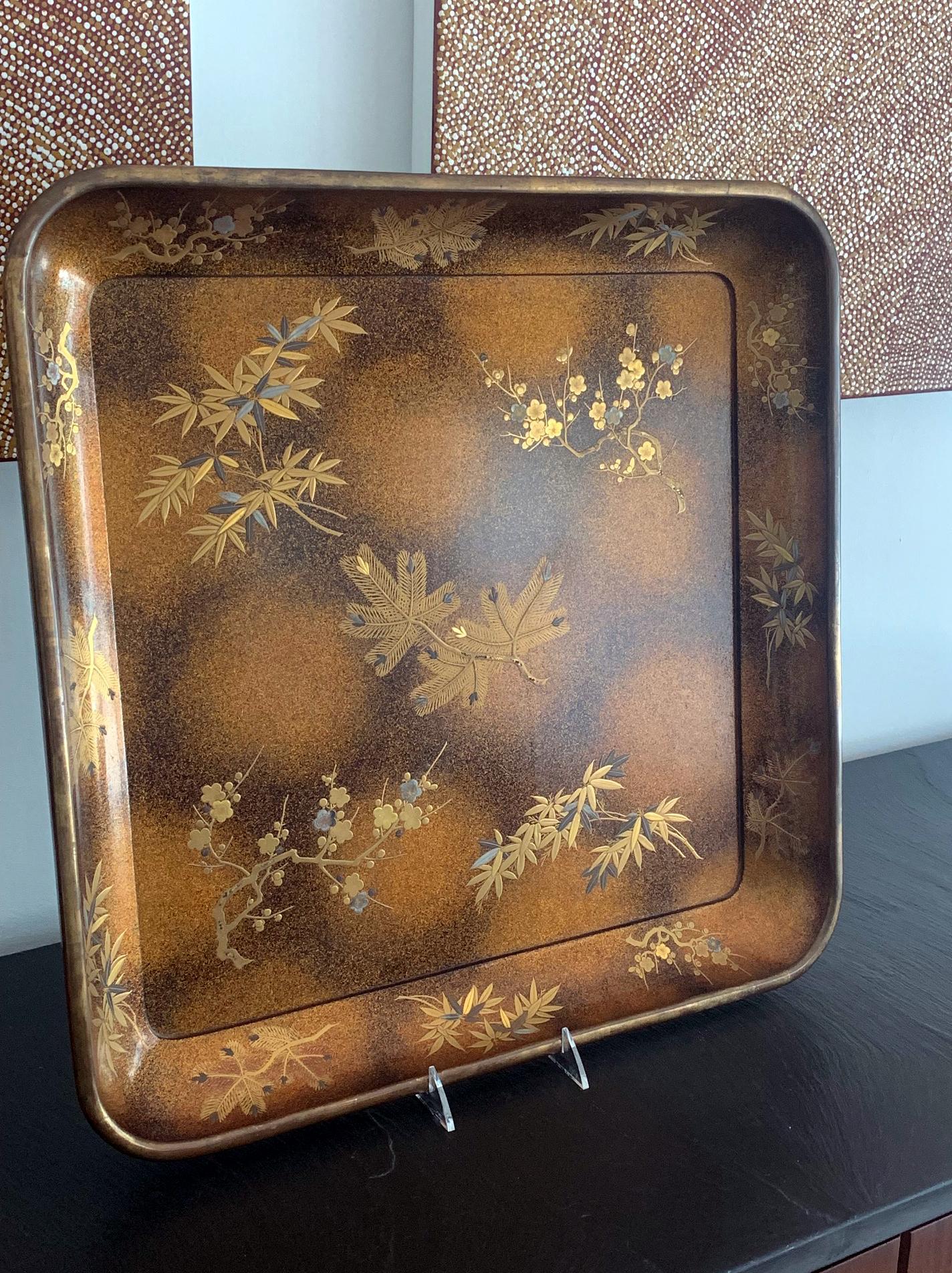 Una gran bandeja cuadrada de presentación lacada (probablemente para kimono) es anterior a 1950 del periodo Showa. Elaboradamente decorado con Maki-e que representa la flor del prunus, bambú y ramas de pino aguja sobre un fantástico fondo moteado