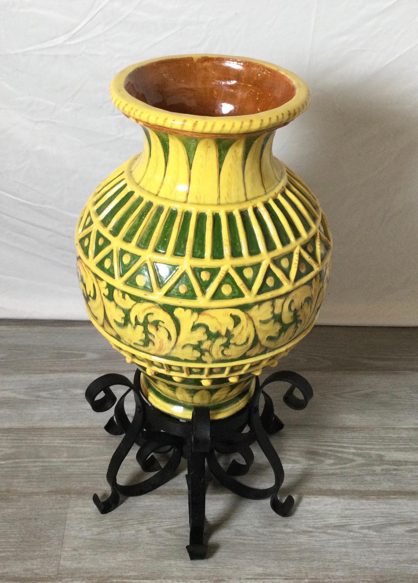 A vibrant yellow and green Italian earthen ware vessel with hand forged wrought iron stand. The glaze is hand decorated with a scrolled acanthus leaf design with a lattice work pattern at the top.
