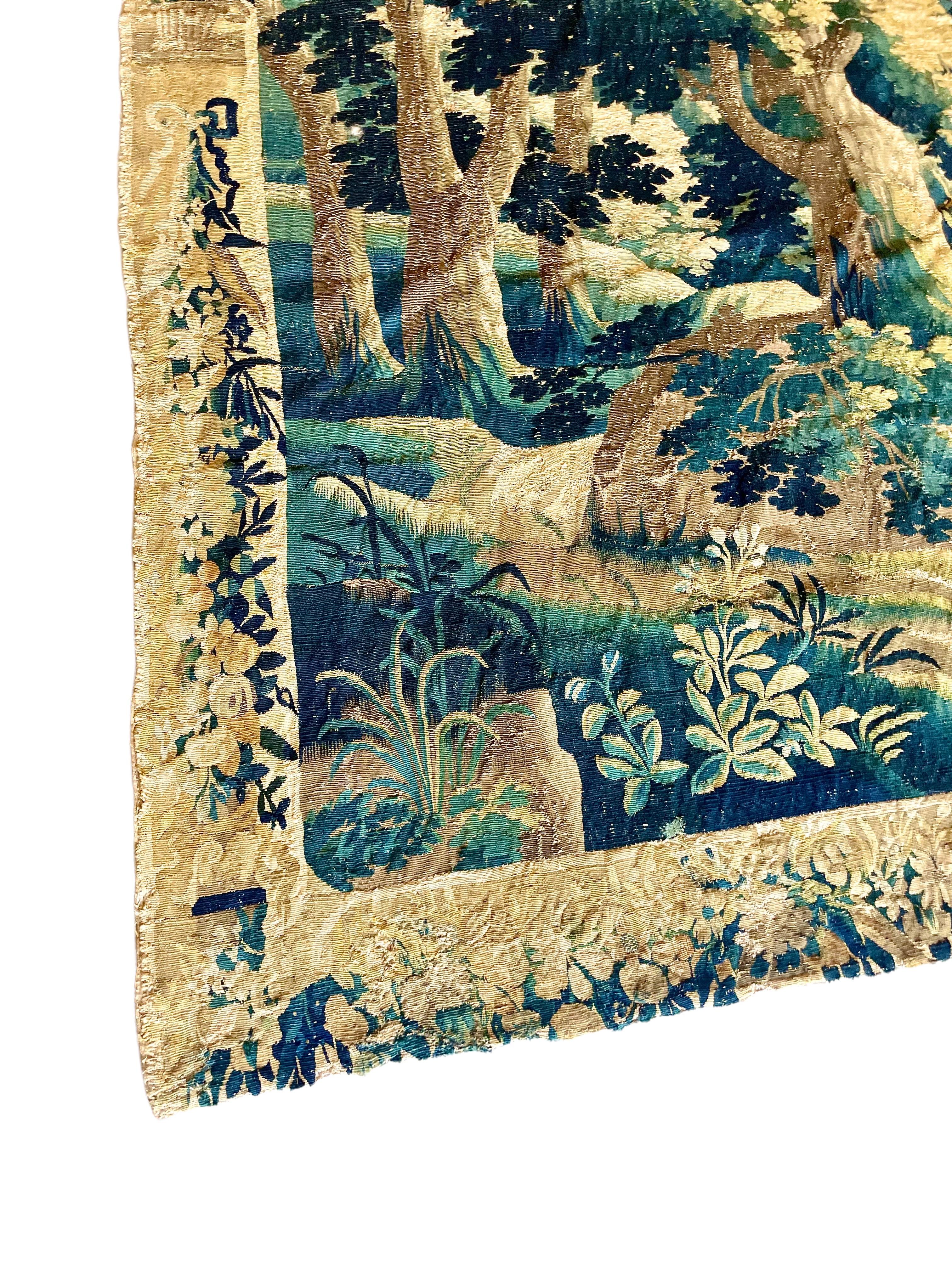 A fine example of an Aubusson 'Verdure' tapestry from the end of the 17th century, depicting a densely wooded landscape, with shrubs and more delicate foliage in the foreground. The tapestry is surrounded by an extravagant floral border. Hand-woven