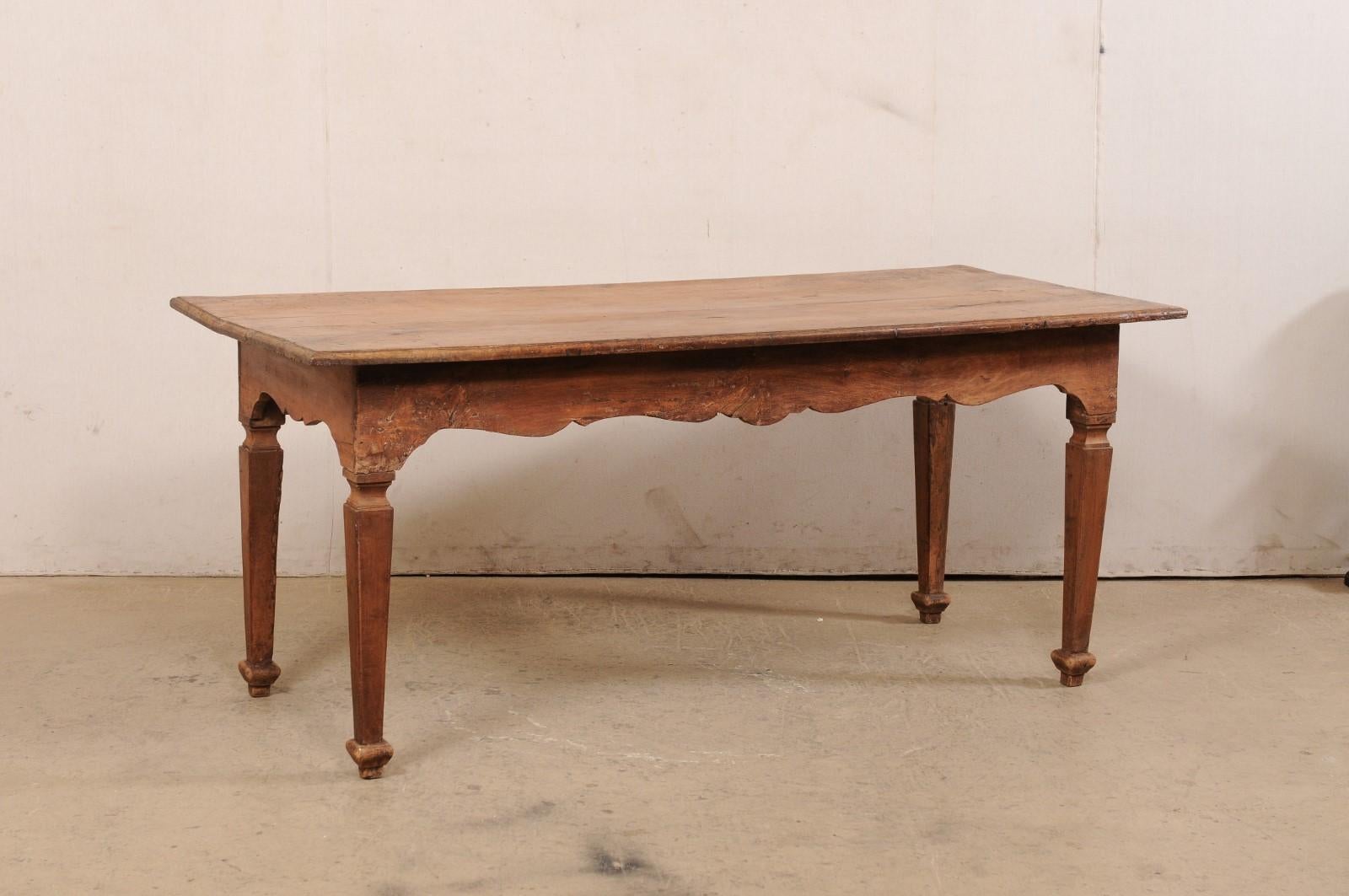 An Italian rustic carved-walnut farm table from the turn of the 18th and 19th century. This antique table from Italy has a rectangular-shaped top which overhangs the apron below which has beautifully carved skirting along all four sides, and is