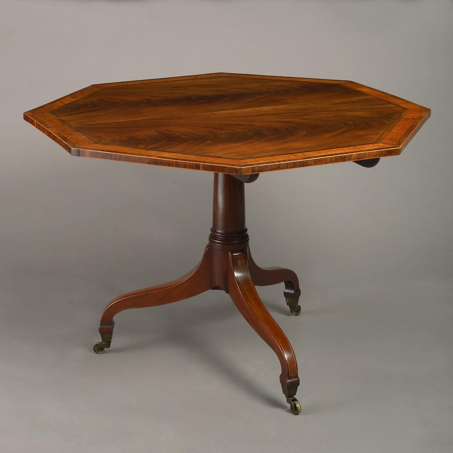 A late 18th century George III Sheraton Period mahogany breakfast or centre table, the top of octagonal form with figured veneers and crossbanding in tulipwood, boxwood and satinwood, all raised on a gun barrel stem with scrolling legs and