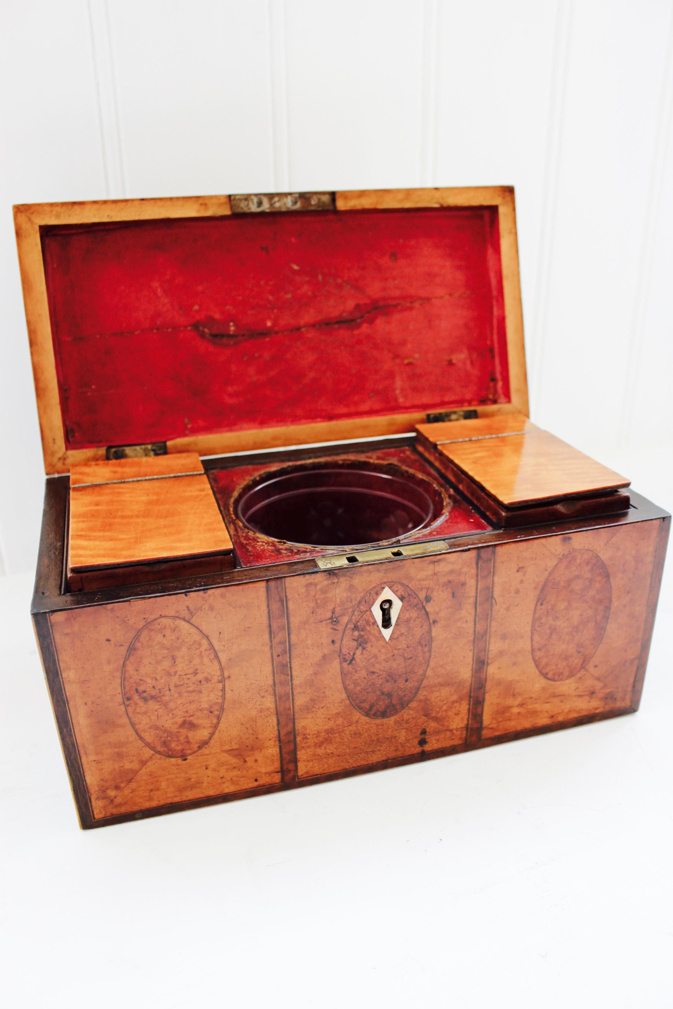 A George III satinwood, amboyna and silver-mounted tea caddy, circa 1780. Rectangular shape, the top and sides with satinwood panels centred on oval amboyna panels, the silver handle with passant lion mark and crest. Internally with twin caddies