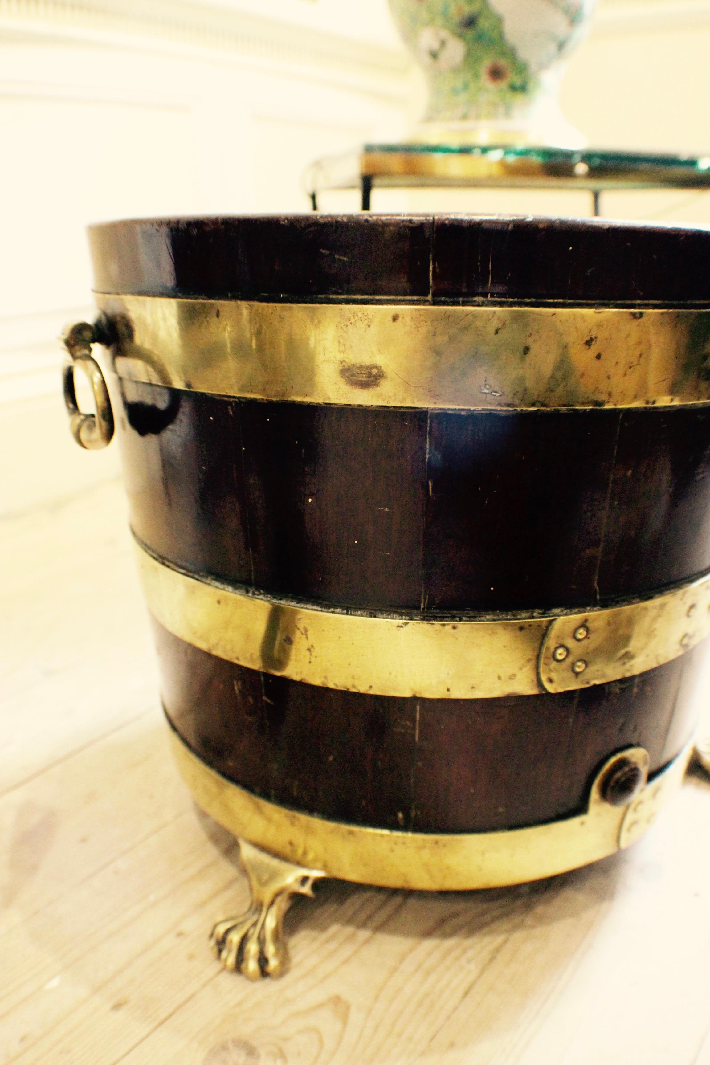 A George III English mahogany and brass bound wine cistern, circa 1780-1800, of tapering cylindrical form, with three brass bands, turned brass handles and three brass lion paw feet.