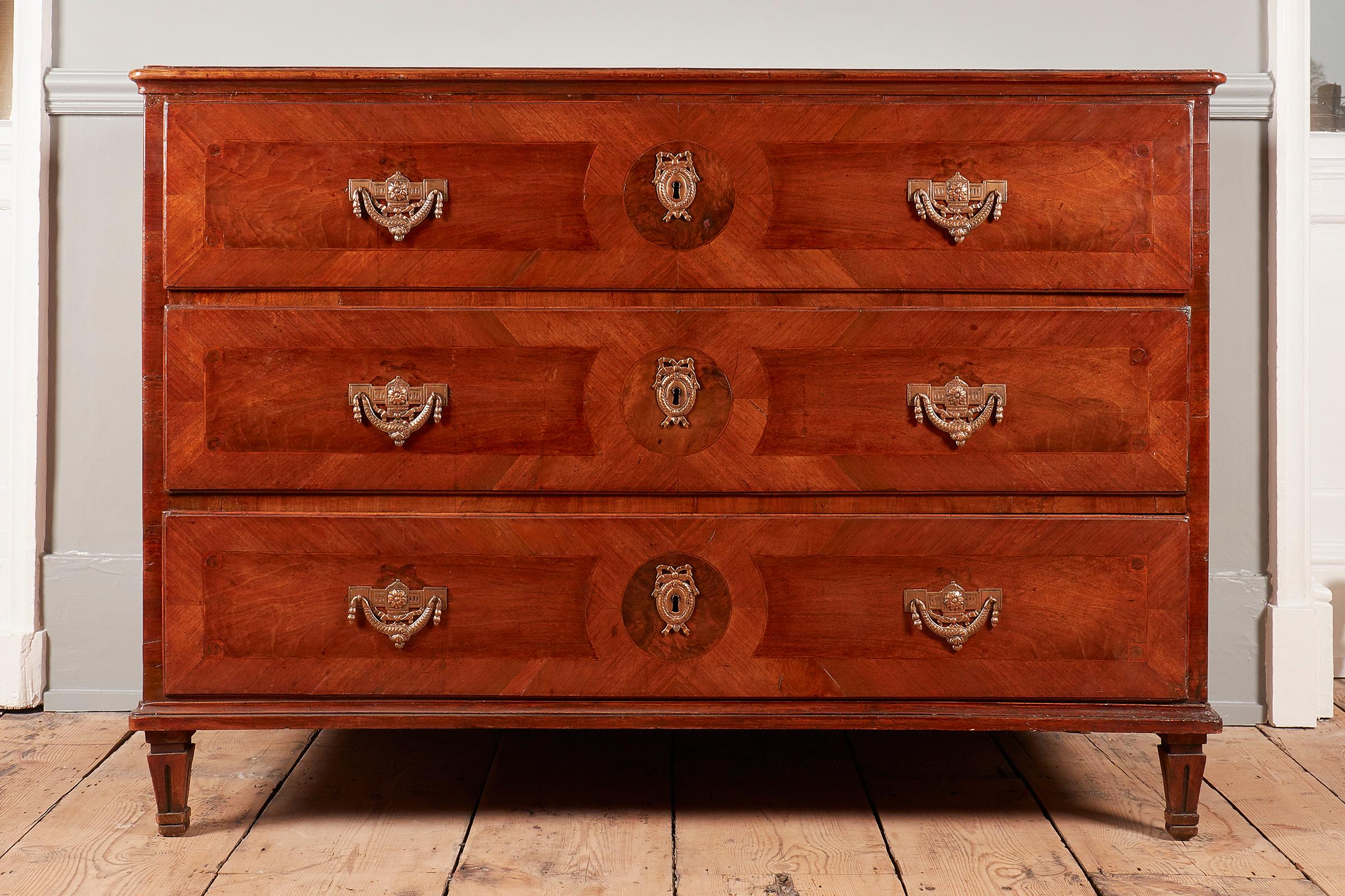 An Italian walnut commode, late 18th century, large proportions, with three drawers, each drawer with escutcheons and handles in brass, on later tapering feet.