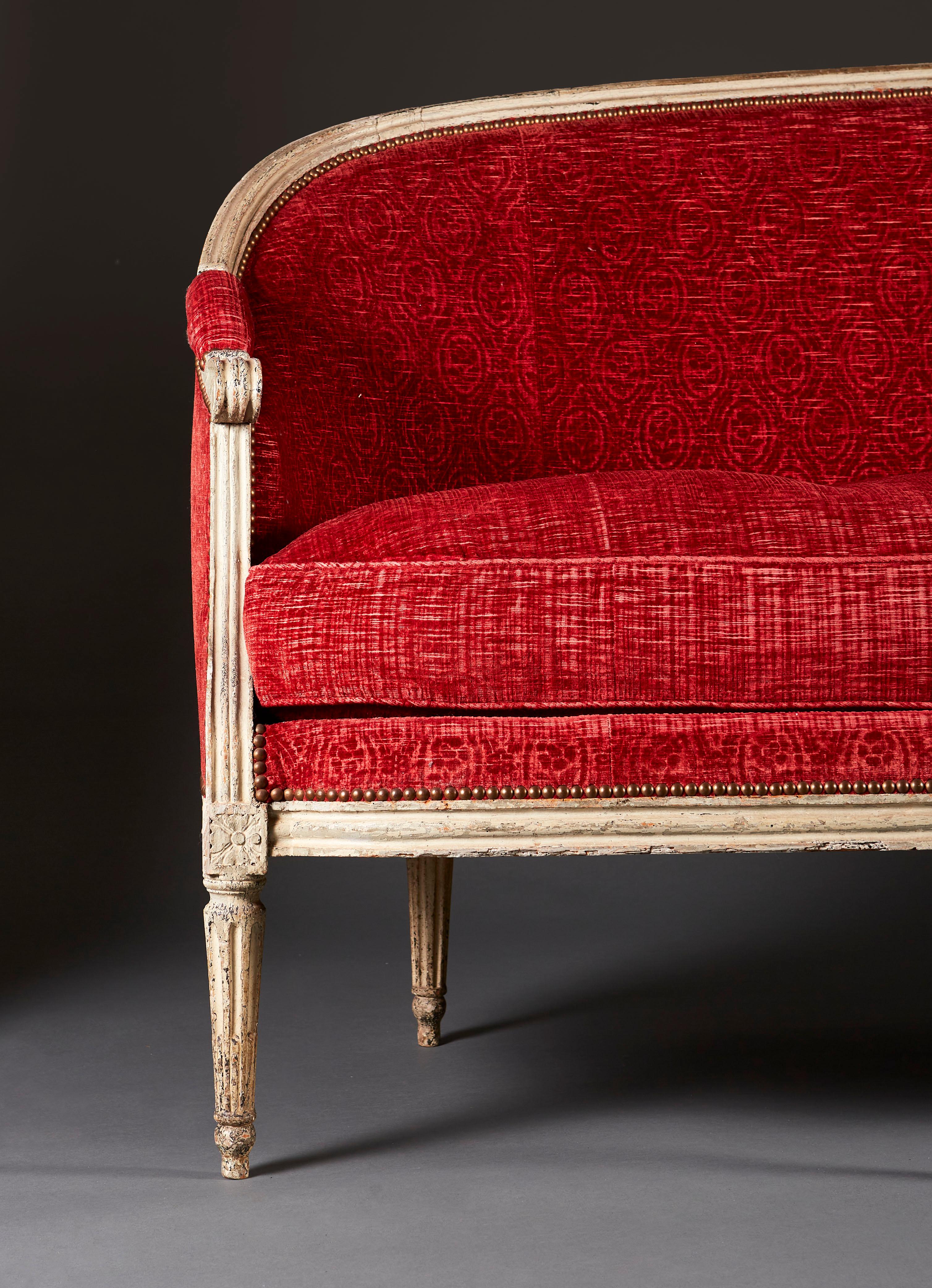 A fine late eighteenth century painted French sofa by Claude Leclerc, with scrolling arms and carved paterae to the seat rail, with crimson cut velvet upholstery and brass studs, all supported on seven fluted tapering legs. Stamped Claude Leclerc.