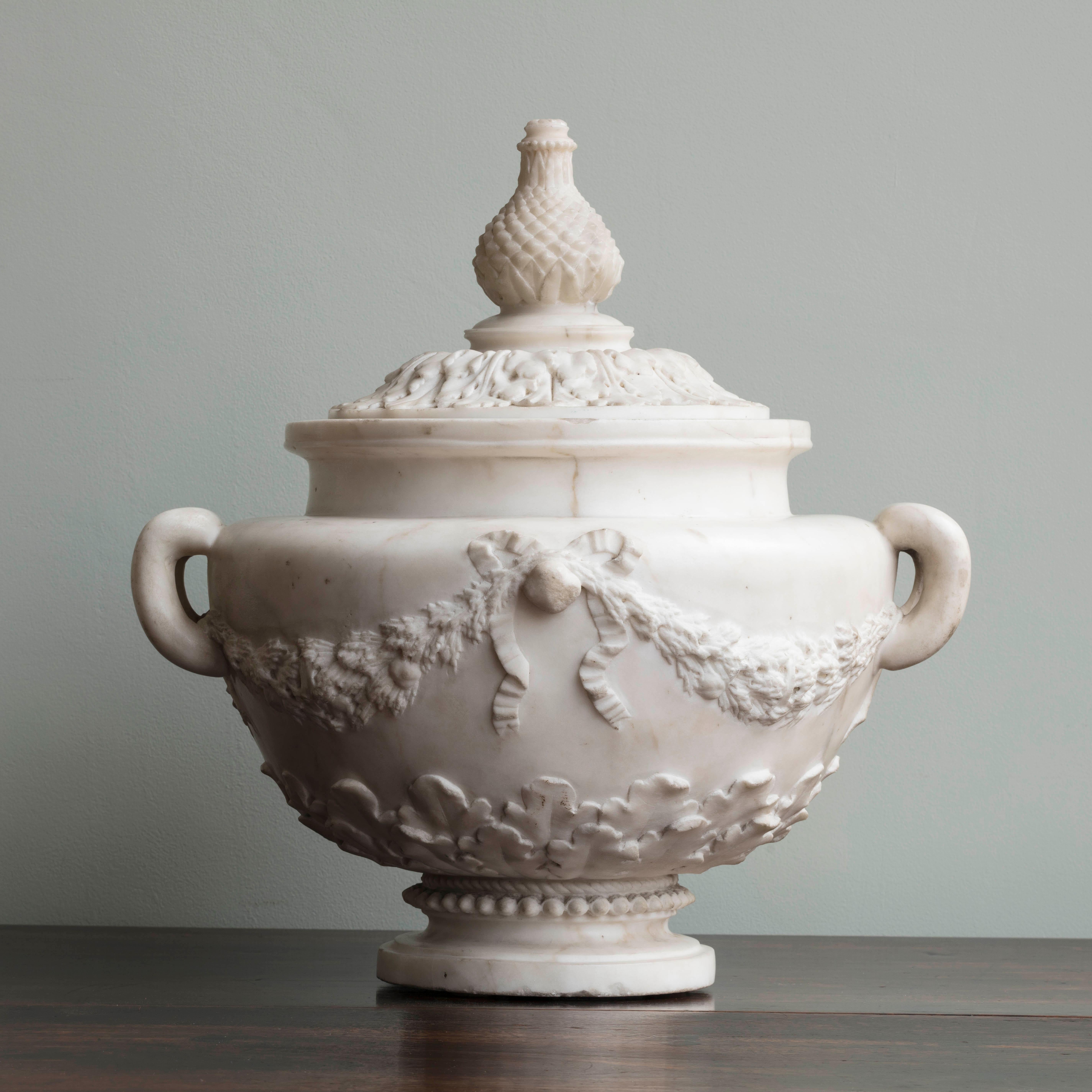 Carved from statuary marble, the removable lid with pineapple finial and acanthus carved cover, above an urn decorated with two pierced handles and carved ribboned swags.
   