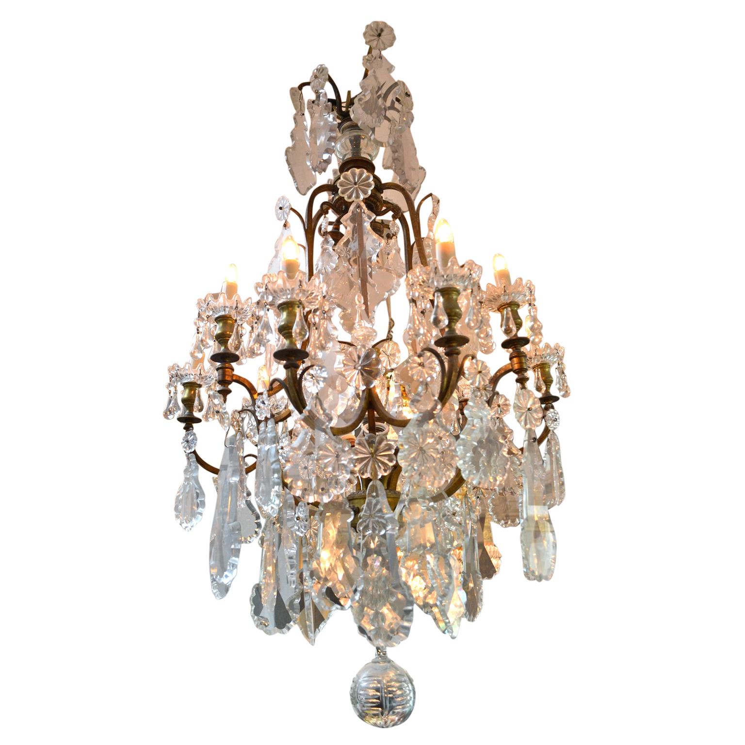 Un lustre classique de style Louis XV en forme de cage d'oiseau avec neuf bras ; la structure en métal doré est lourdement chargée de plaquettes en cristal de différentes tailles ; à l'origine éclairé par des bougies mais maintenant complètement