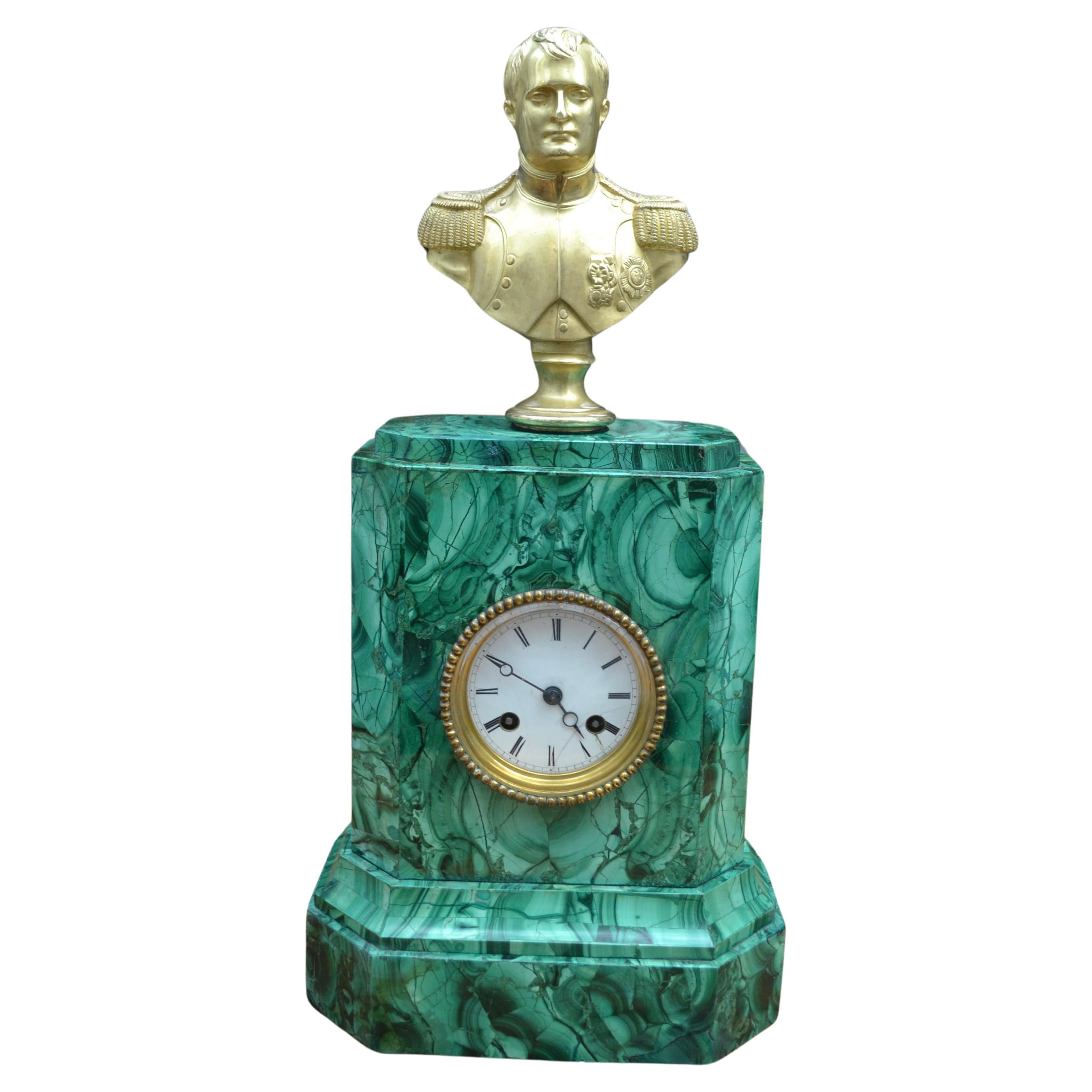 Un sencillo pero elegante reloj con caja de malaquita, relativamente raro, rematado por un busto de bronce dorado de un joven Napoleón en uniforme, según la obra original en mármol de  Jean Antoine Houdon.