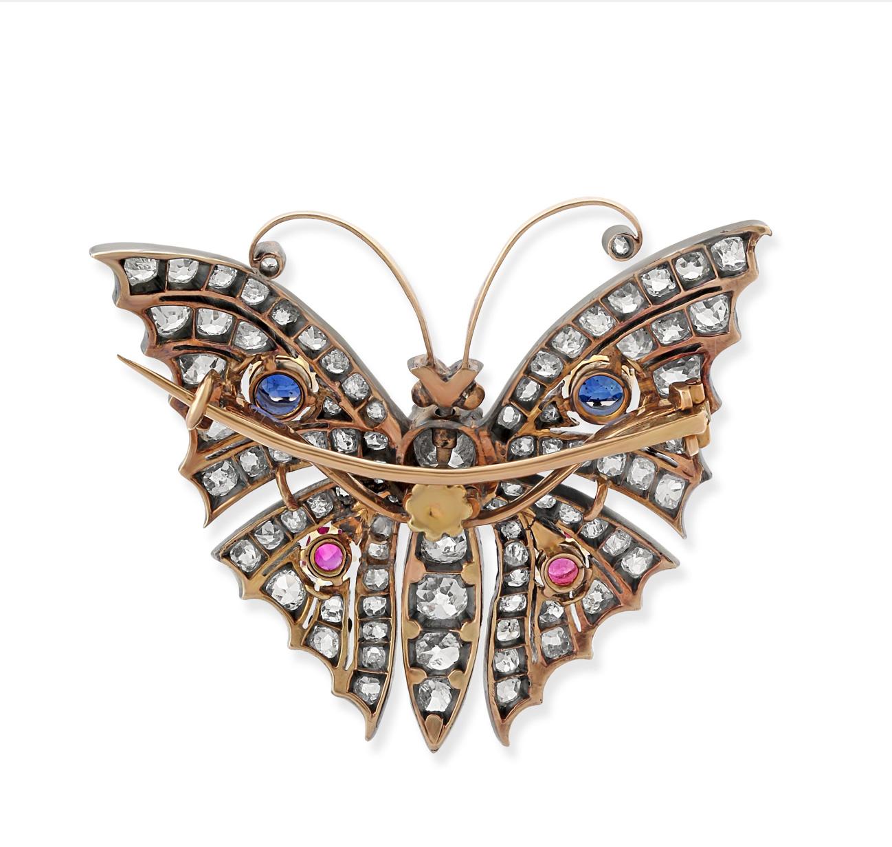 A Late 19th Century butterfly brooch. Set with approximately 7 carats of cushion shape, old and brilliant-cut diamonds with sapphire and rubies mounted in silver on top of gold. Length = 39mm.
