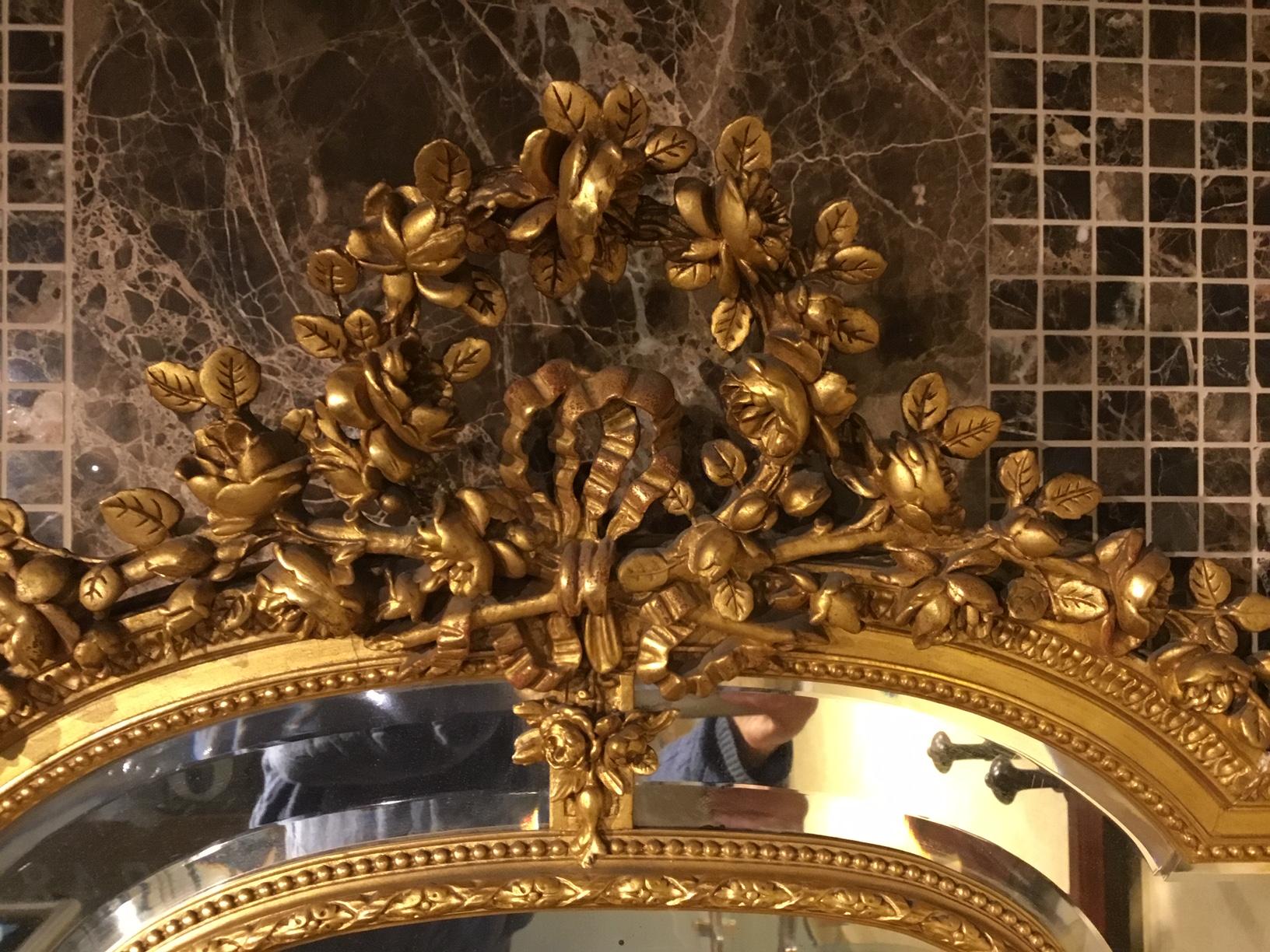 A Late 19th Century French Carved Gilt-wood & gesso margin mirror. The elaborately carved gilt-wood and gesso frame with a wonderful floral crest flanked by twin flaming urns with a central shaped bevelled mirror, with further margin mirrors to the